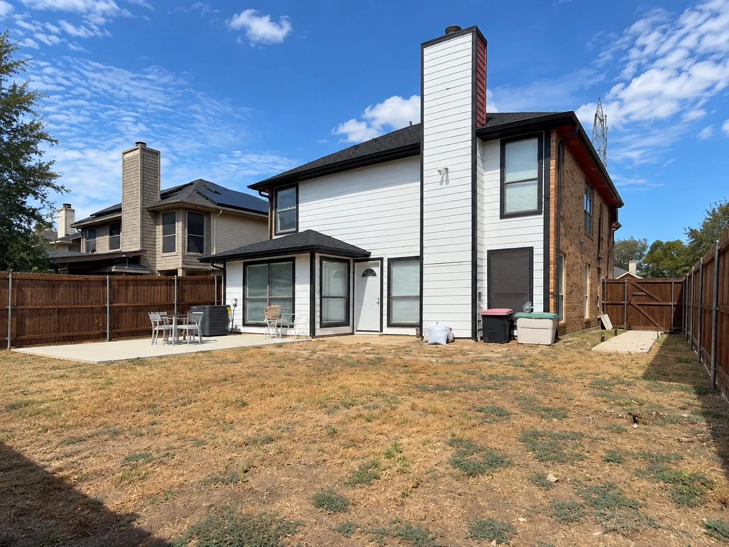 Expansive backyard featuring a concrete patio, wood fencing, and a white siding exterior with brick accents