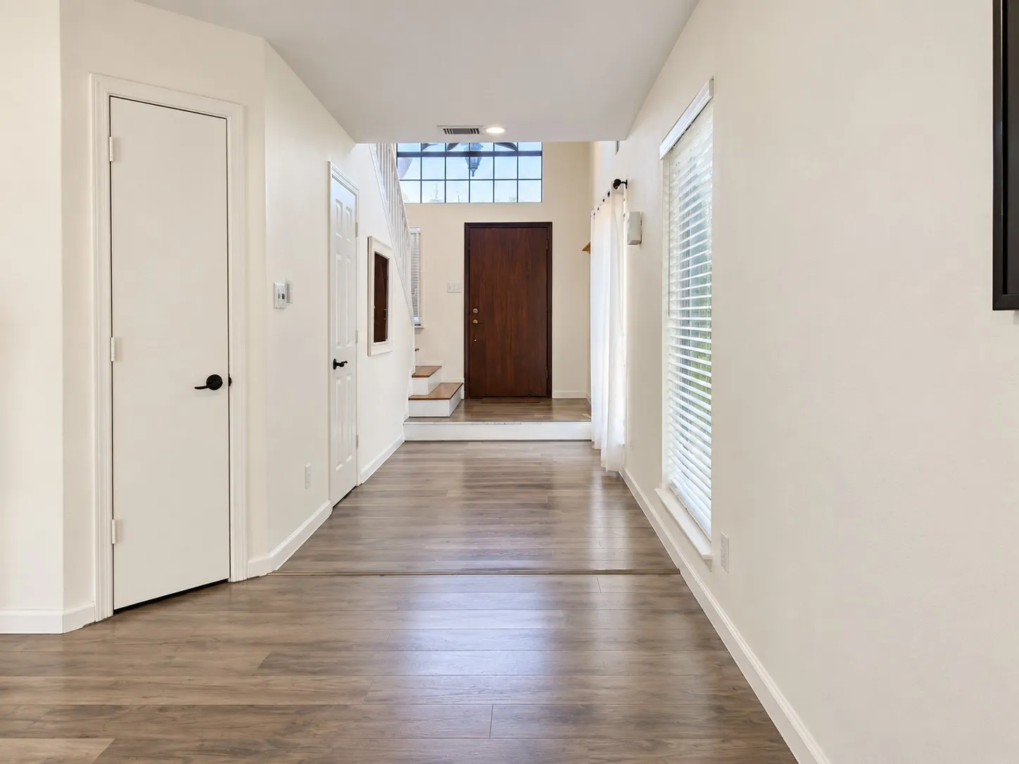 Wood-finish flooring throughout, white interior doors with matte black hardware, and an entryway with a prominent wood-panel door and transom window