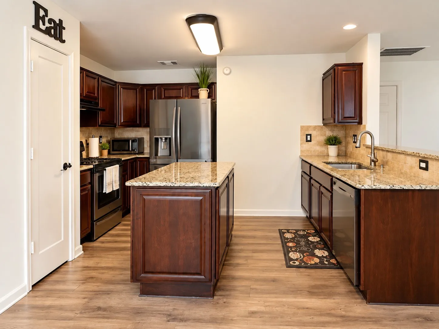 Kitchen featuring wood-finish flooring, dark wood cabinetry, granite countertops, and stainless steel appliances