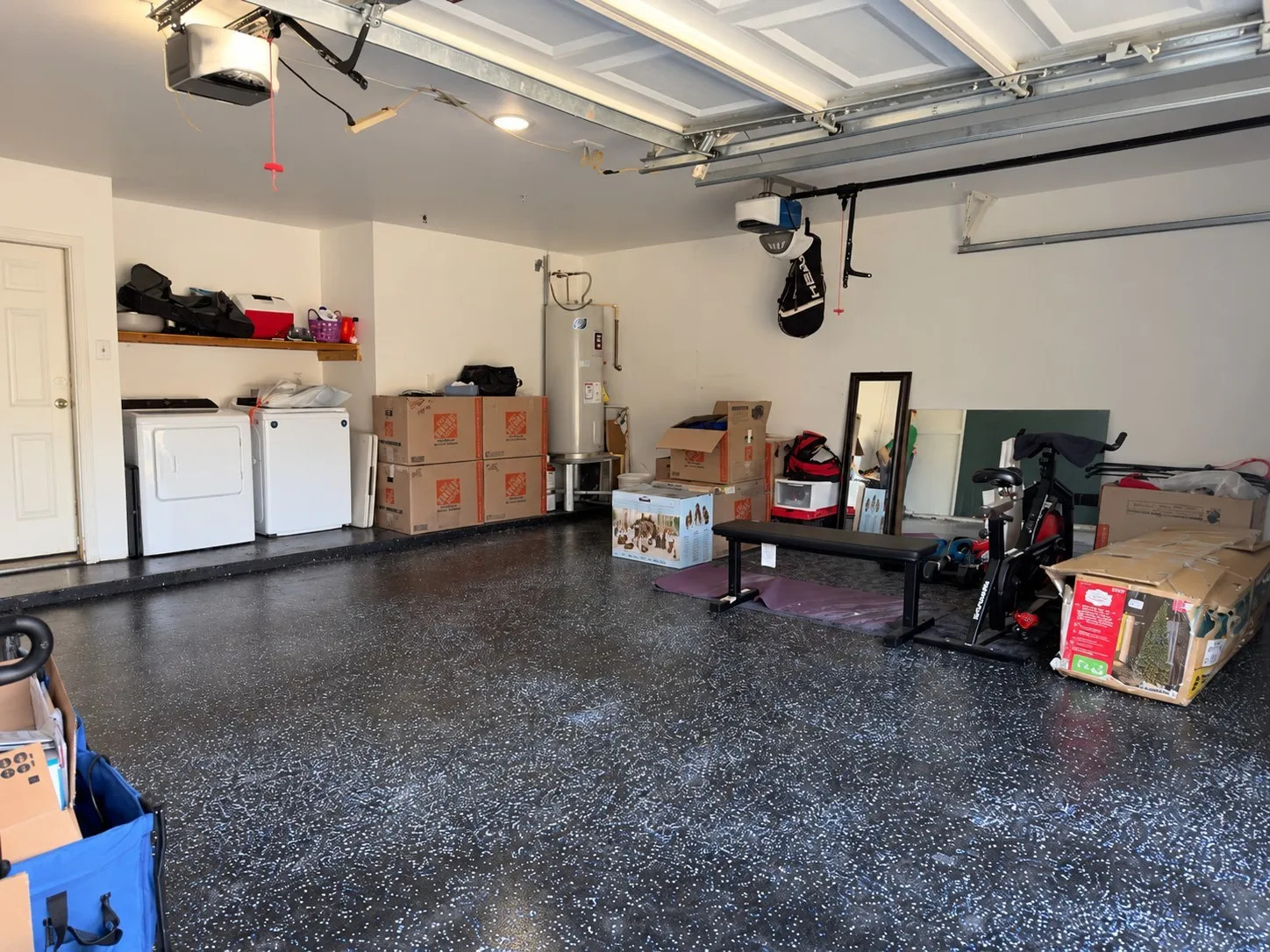 Garage with a durable epoxy-coated floor, overhead garage door opener, built-in shelving, and utility hookups