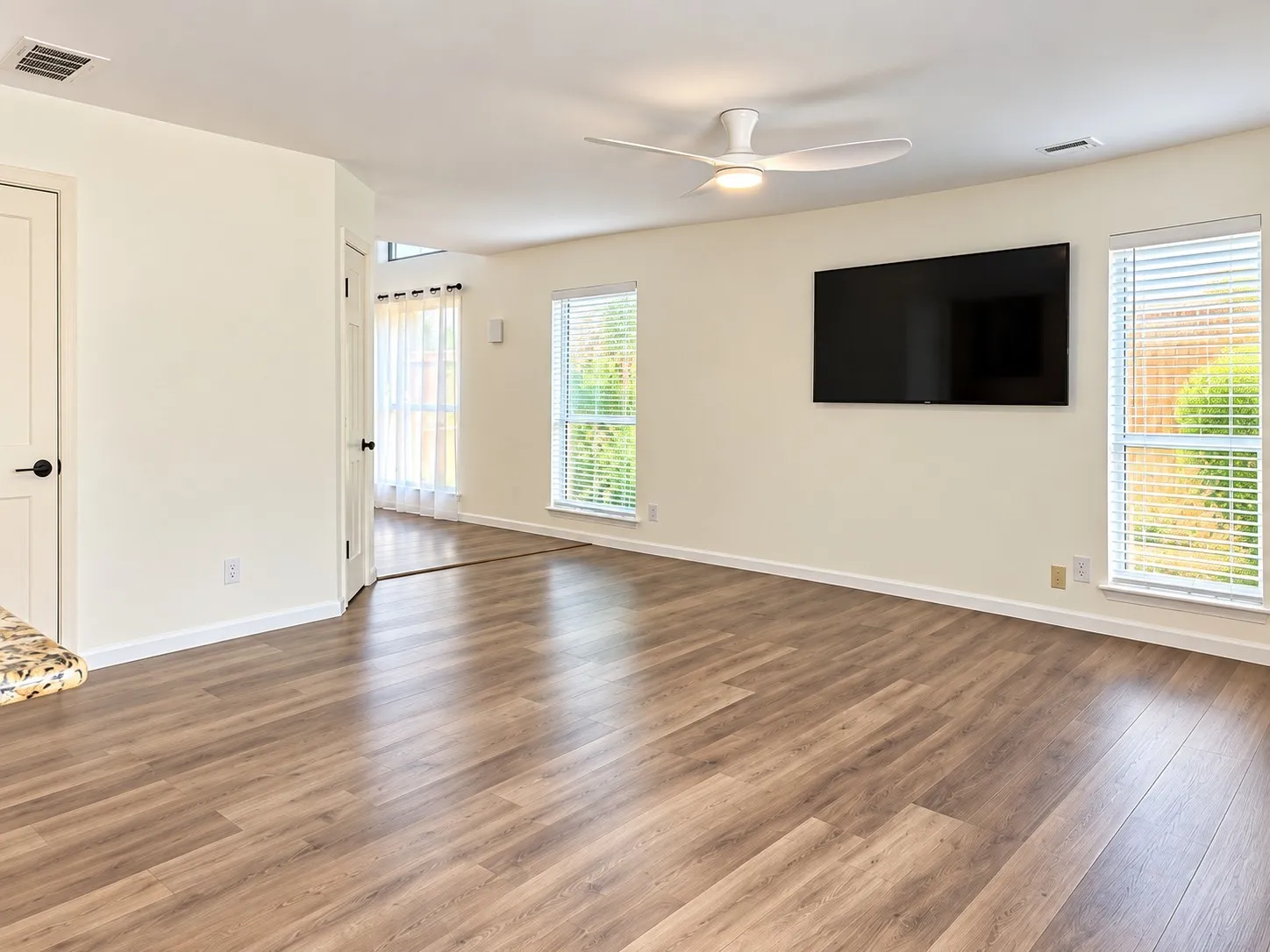 Spacious room with wood-finish flooring, light-toned walls, and a ceiling fan