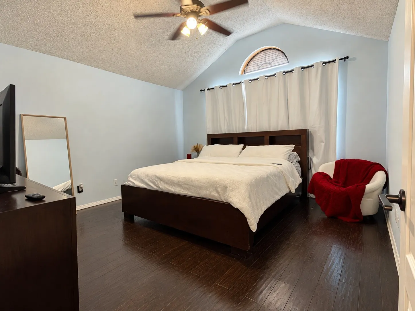 Vaulted ceiling with a ceiling fan, dark wood-finish flooring, and an arched transom window