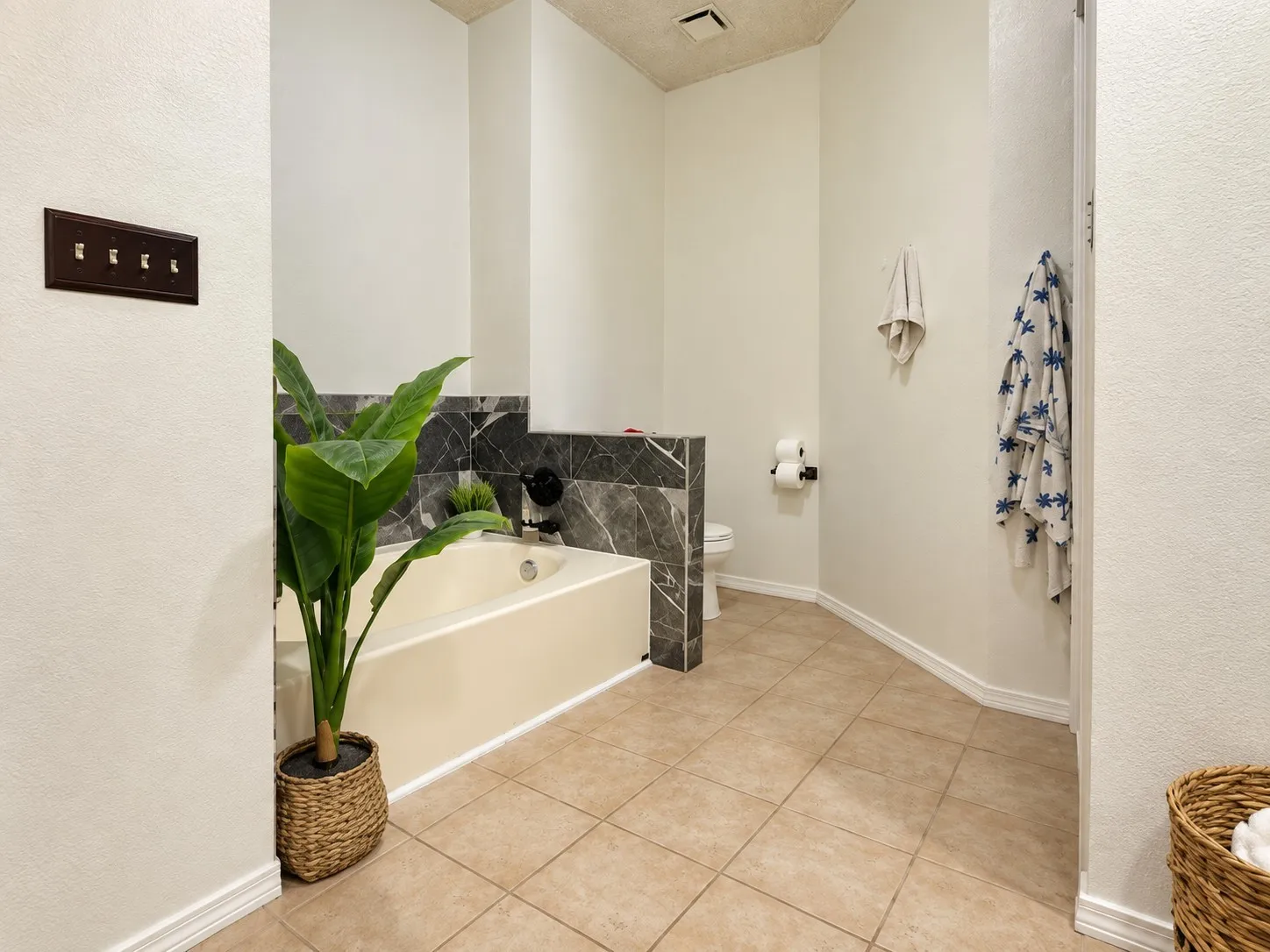 Soaking tub with a dark stone surround, matte black fixtures, tile flooring, and a white toilet