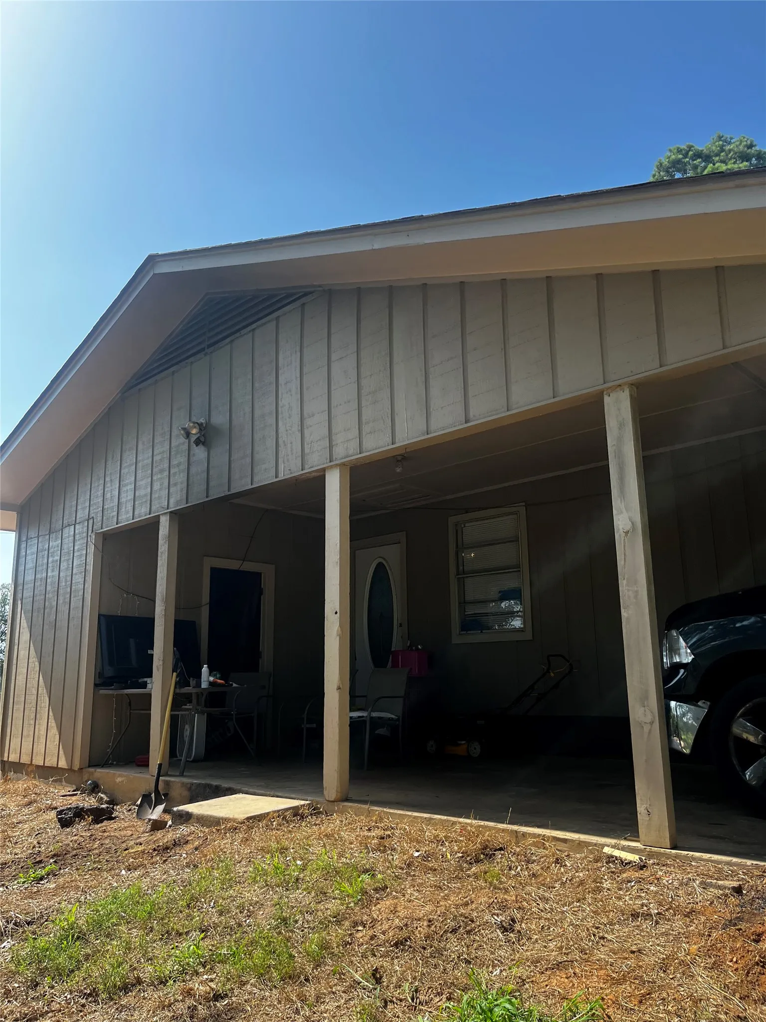 Covered carport with vertical siding, a pitched roof, and a visible front entry door