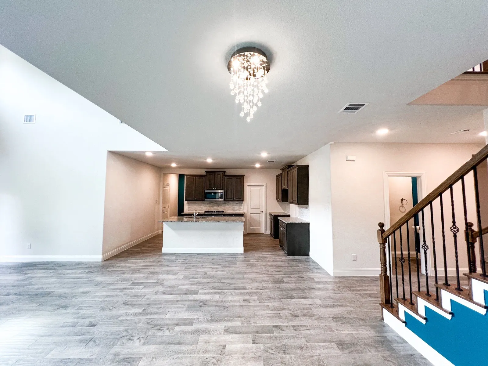 Spacious interior featuring wood-finish flooring, a contemporary chandelier, recessed lighting, and a kitchen with dark cabinetry and a central island