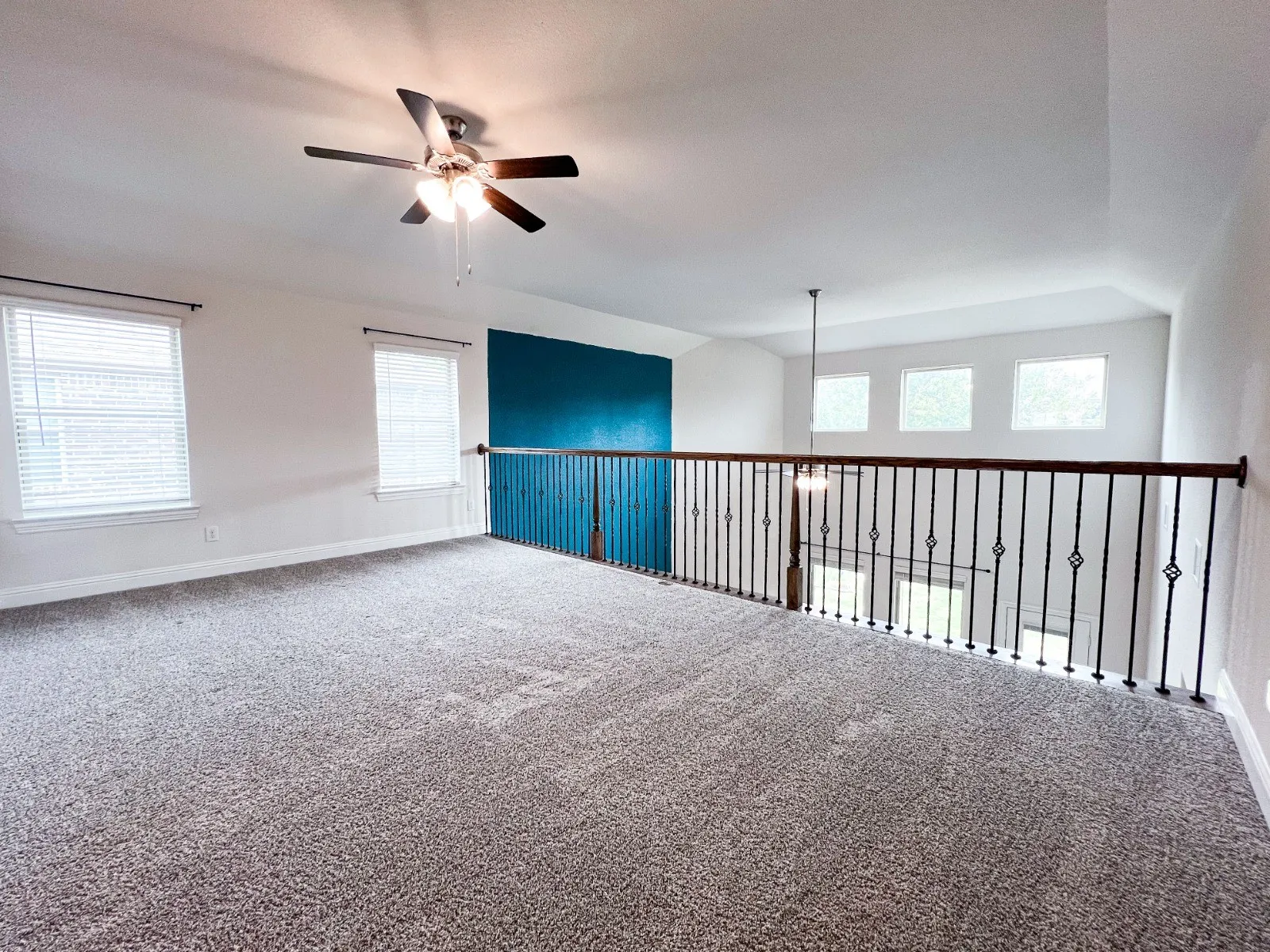 Spacious carpeted loft with an accent wall, three windows, and a ceiling fan with integrated lighting