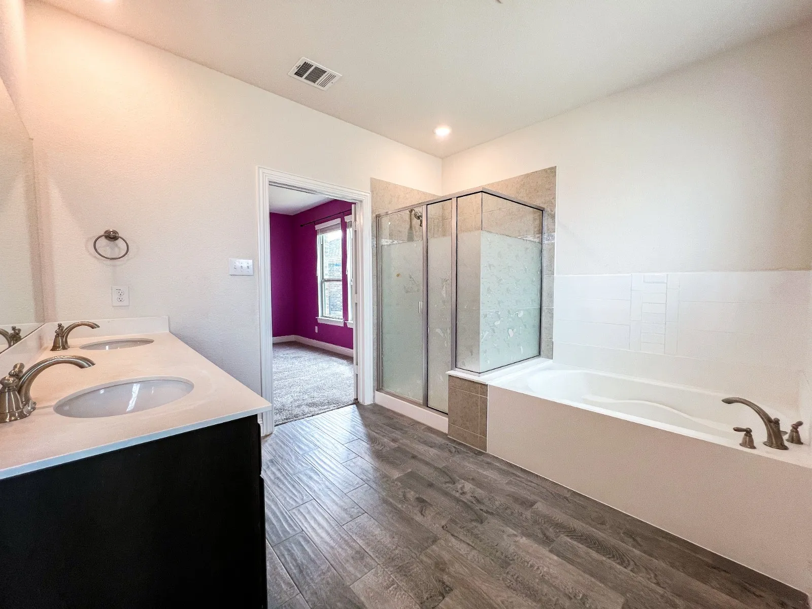 Dual vanity with undermount sinks, wood-finish flooring, glass-enclosed shower, and built-in soaking tub