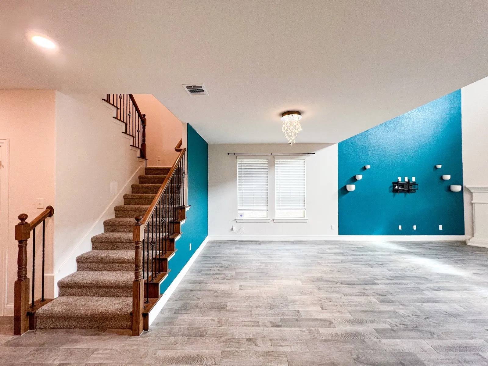 Wood-finish flooring, carpeted staircase with wood handrails, decorative accent wall, built-in wall decor, and a crystal chandelier