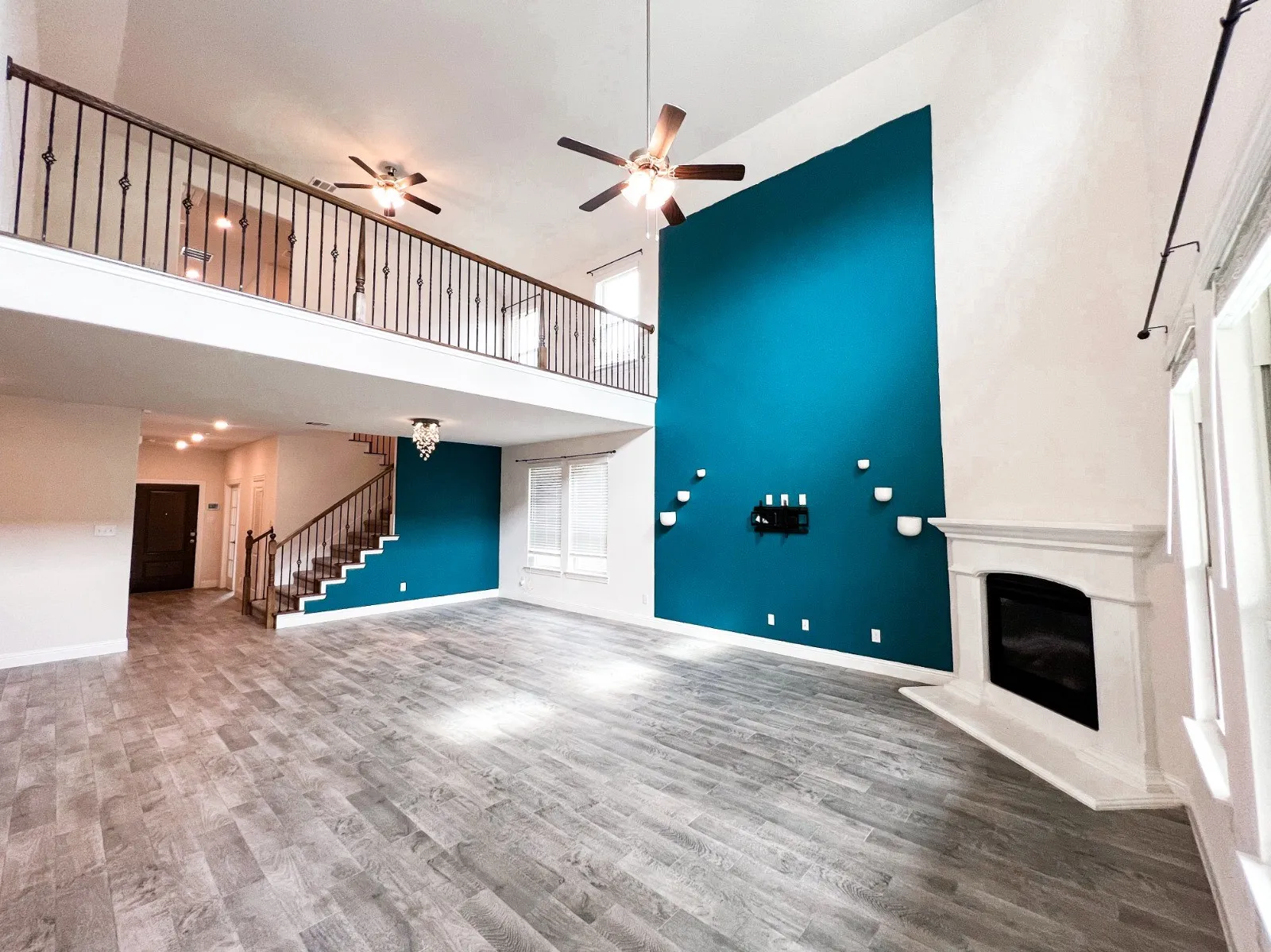 Expansive living area featuring soaring ceilings, wood-finish flooring, a decorative fireplace, and a second-story interior balcony with wrought iron railing