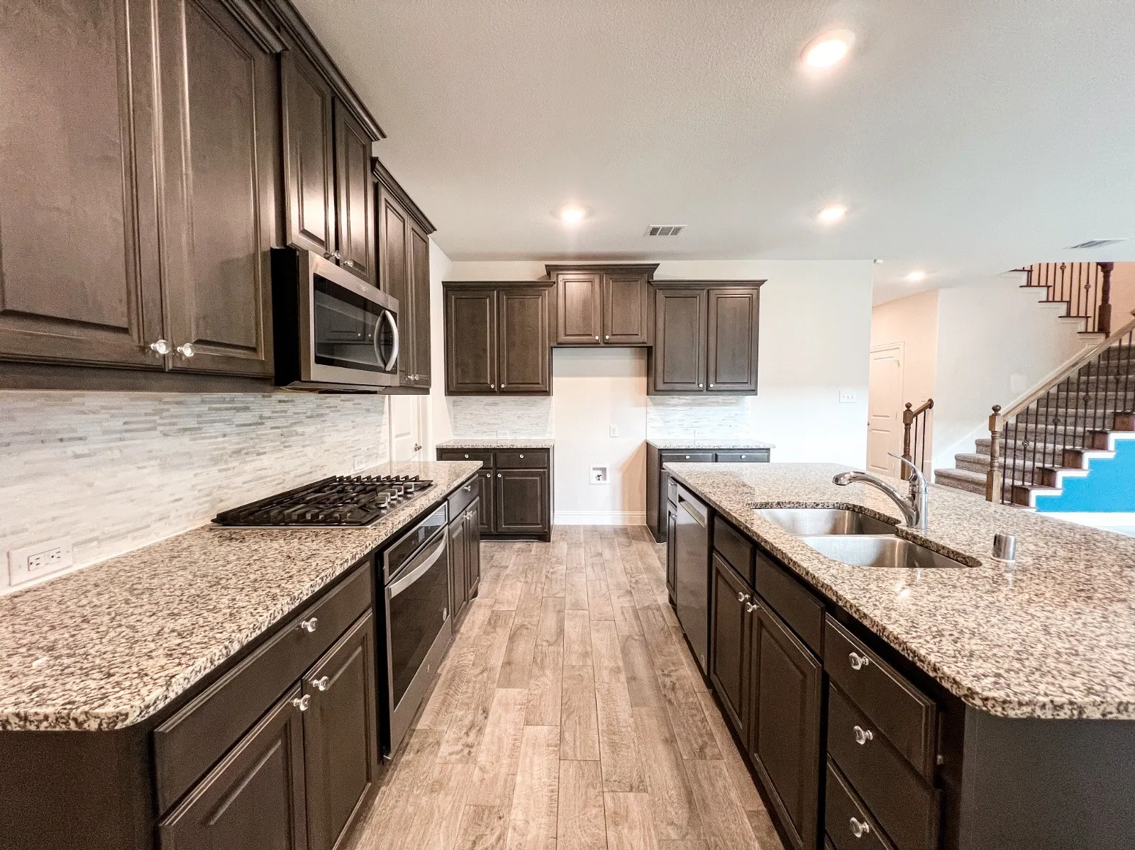 Kitchen with wood-finish flooring, dark wood cabinetry, granite countertops, and a tile backsplash