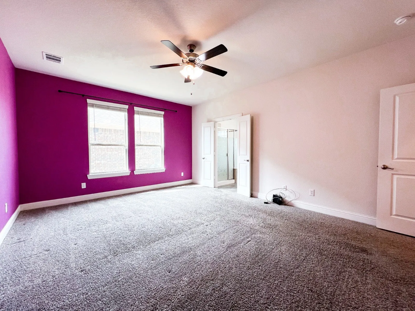 Spacious room with gray textured carpeting, ceiling fan with integrated lighting, two windows, and a doorway leading to a separate area