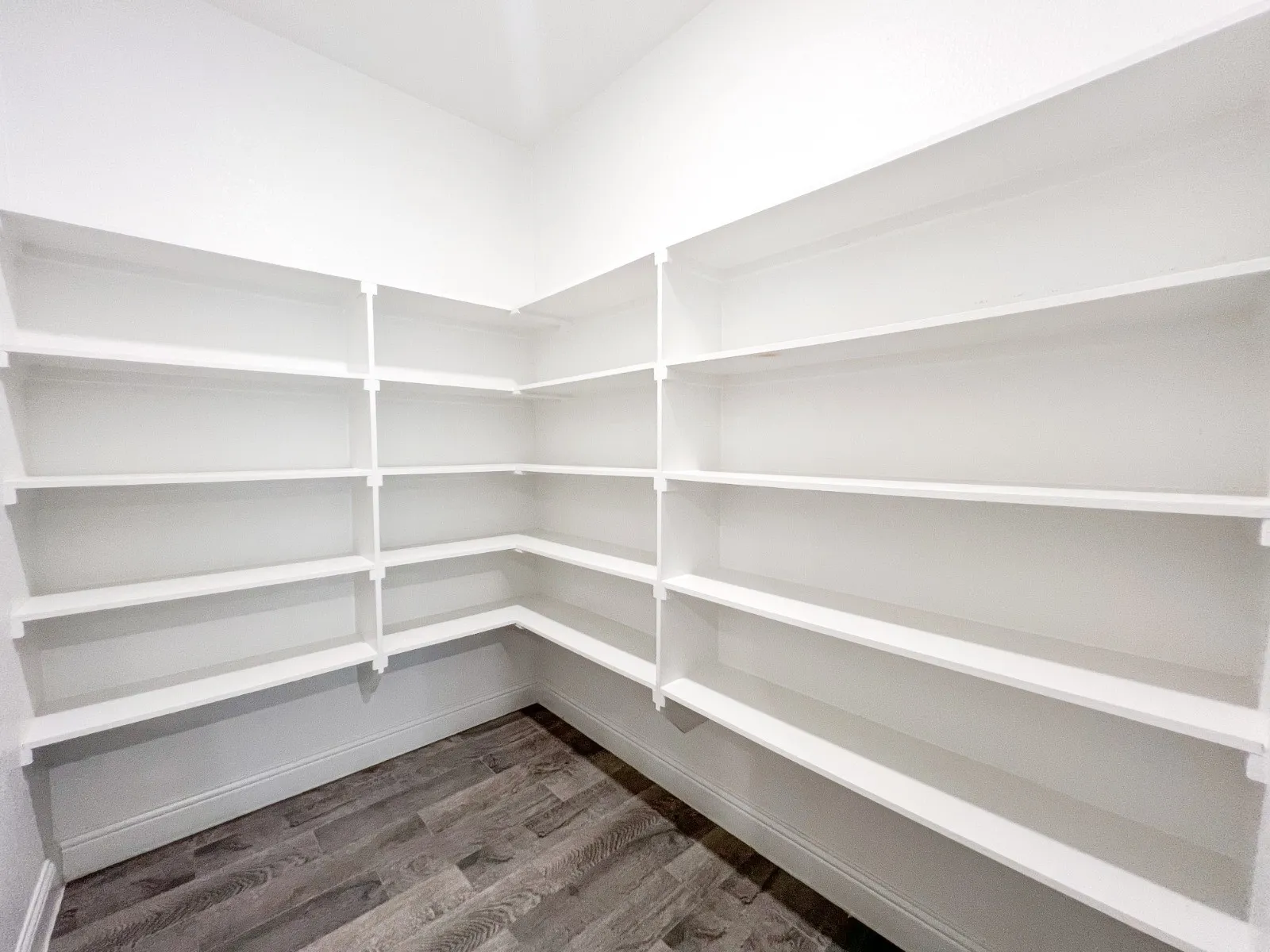 Floor-to-ceiling white shelving providing extensive storage, corner configuration, and wood-finish flooring