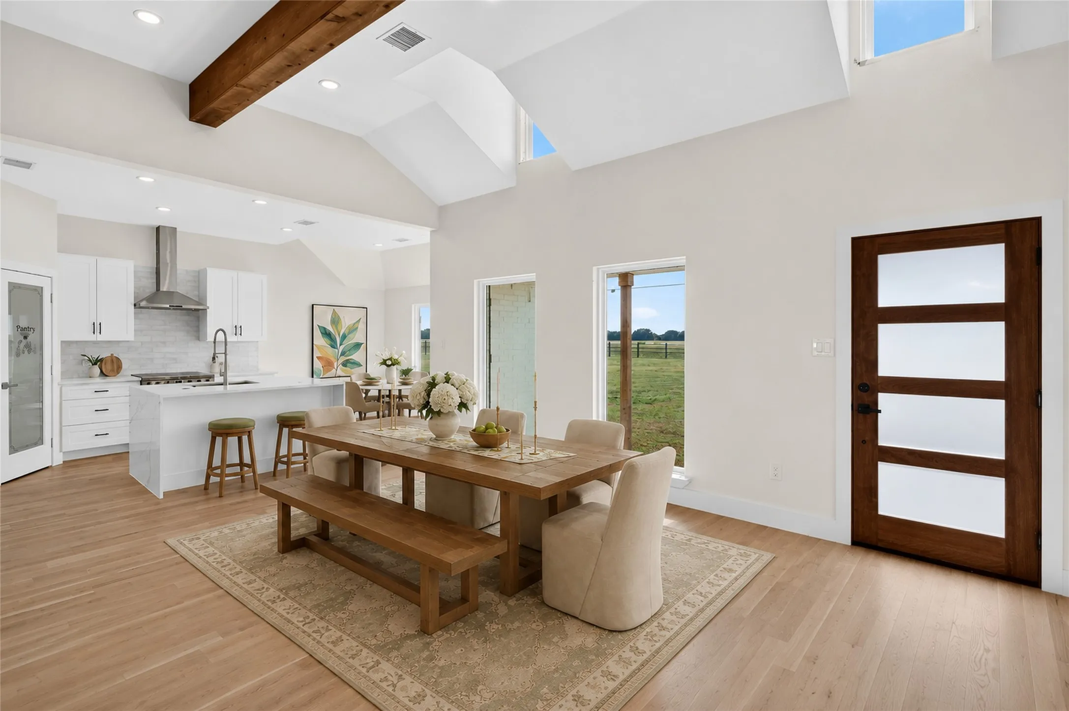 Open-concept living space featuring vaulted ceilings with exposed wood beams, light wood-finish flooring, and white walls - Virtually Staged