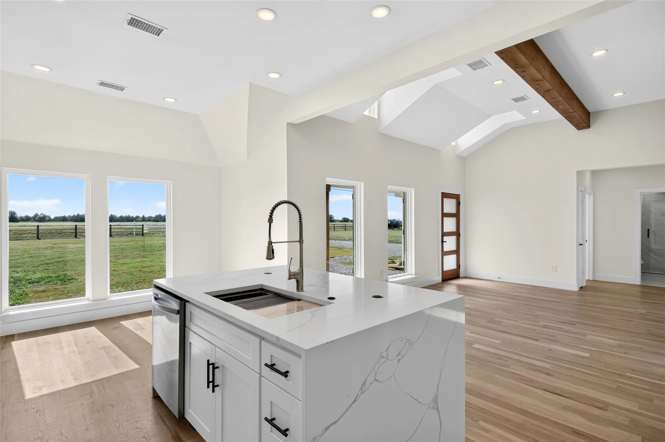 Spacious open-concept interior featuring light wood-finish flooring and vaulted ceilings with exposed wood beams