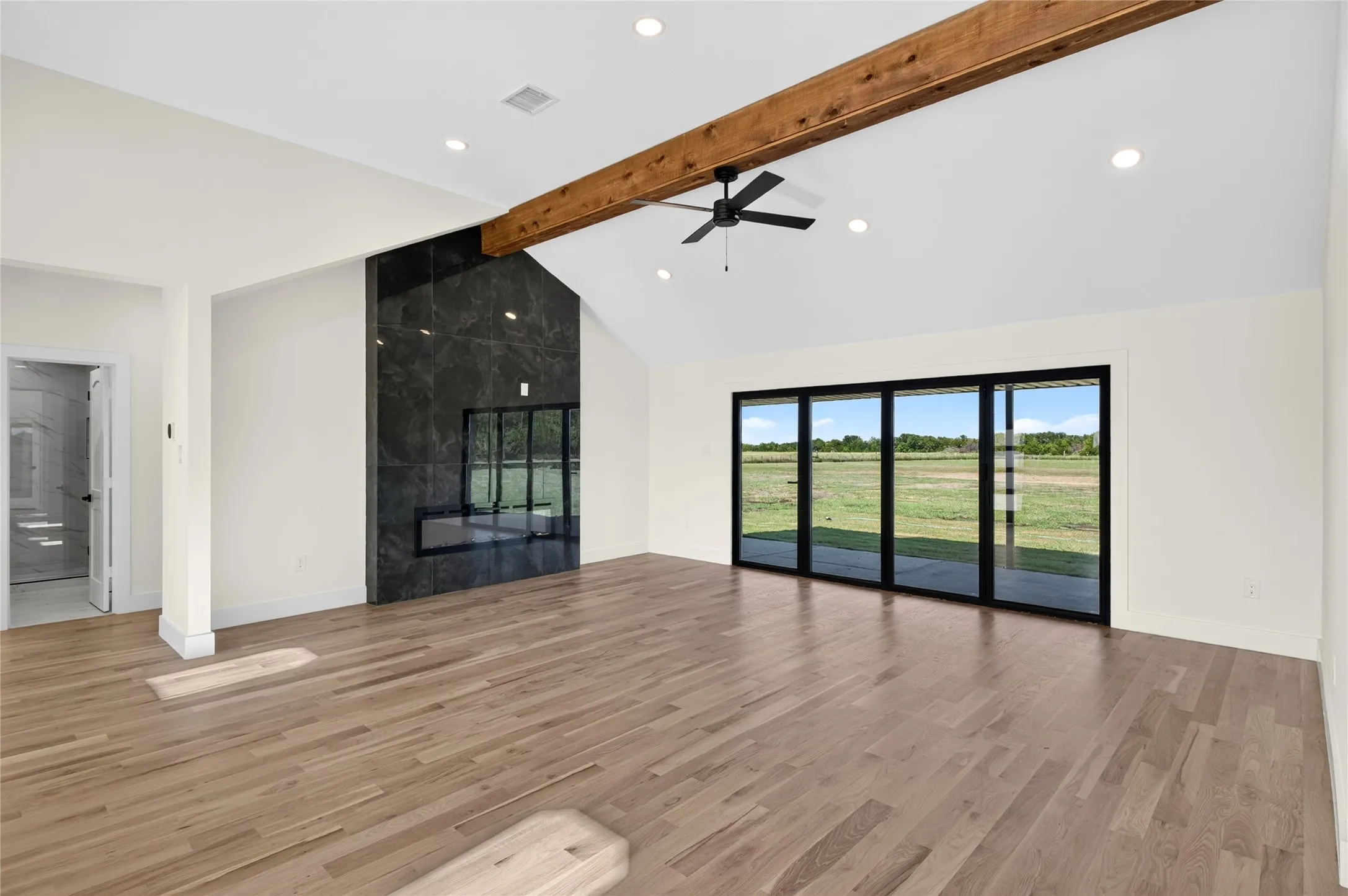 Spacious living area featuring high vaulted ceilings, light wood-finish flooring, and a striking dark stone fireplace