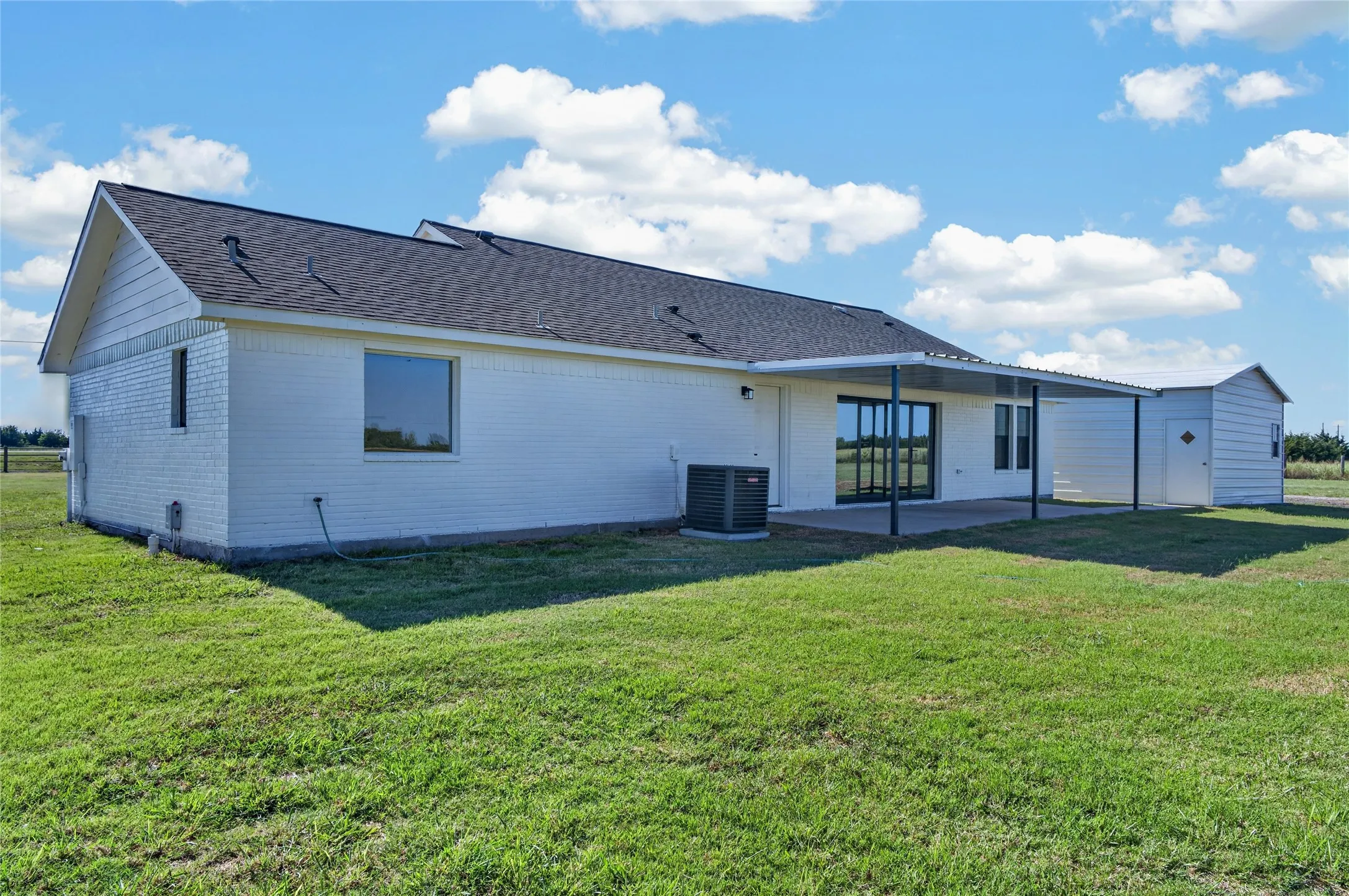 White brick exterior with an attached covered patio featuring a concrete slab and a detached storage shed