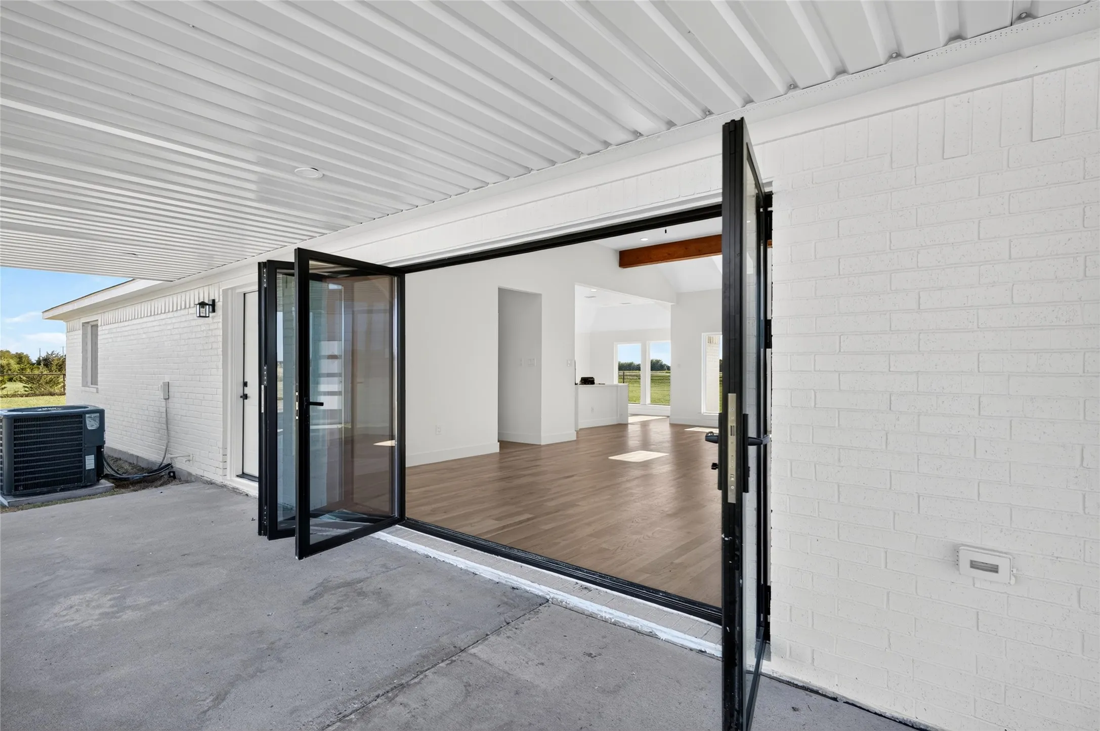 Covered concrete patio with bi-fold glass doors opening to an interior space featuring wood-finish flooring and white walls