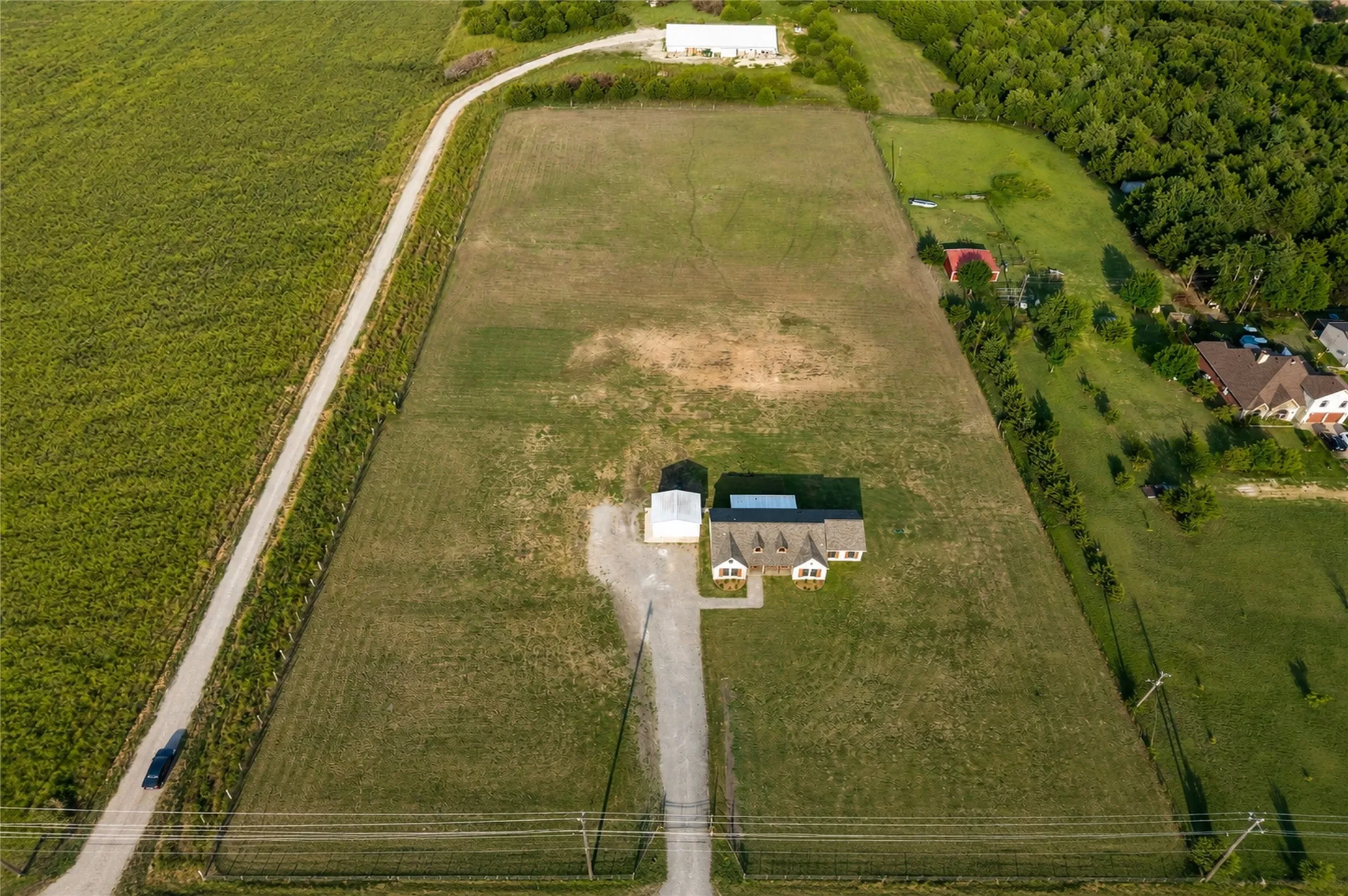 Expansive land parcel featuring a residential structure, detached outbuilding, gravel driveway, and surrounding green fields