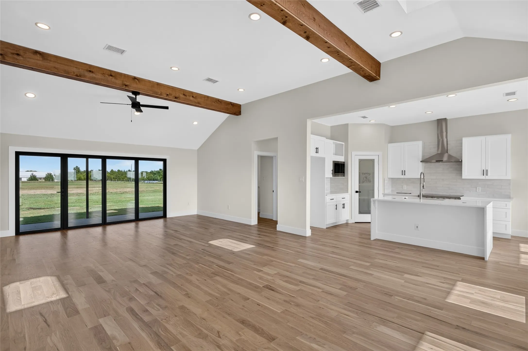 Spacious living area featuring high vaulted ceilings with exposed wood beams, wood-finish flooring, and a contemporary ceiling fan