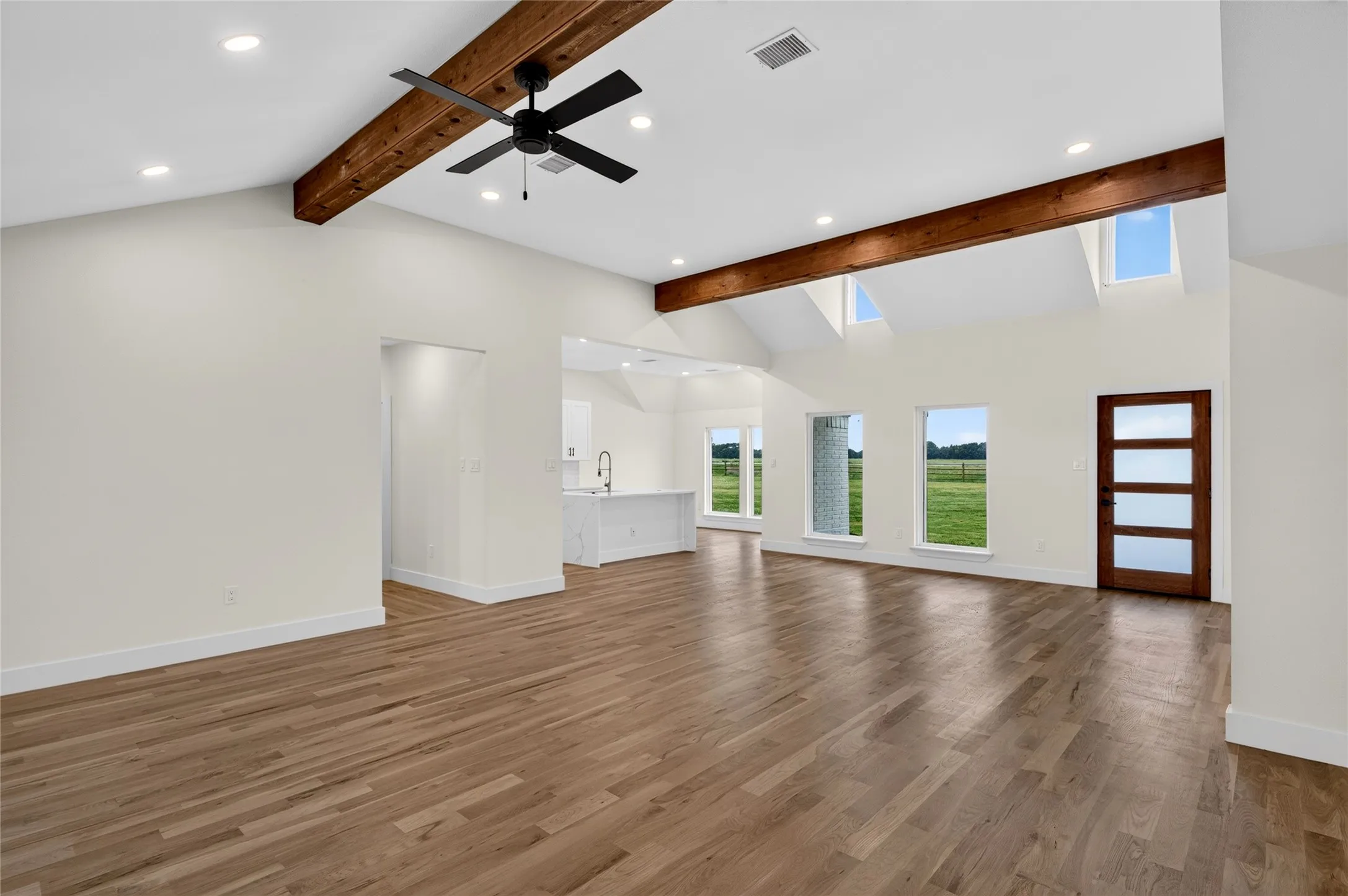 Spacious living area featuring wood-finish flooring, exposed ceiling beams, a contemporary ceiling fan, recessed lighting, and multiple windows