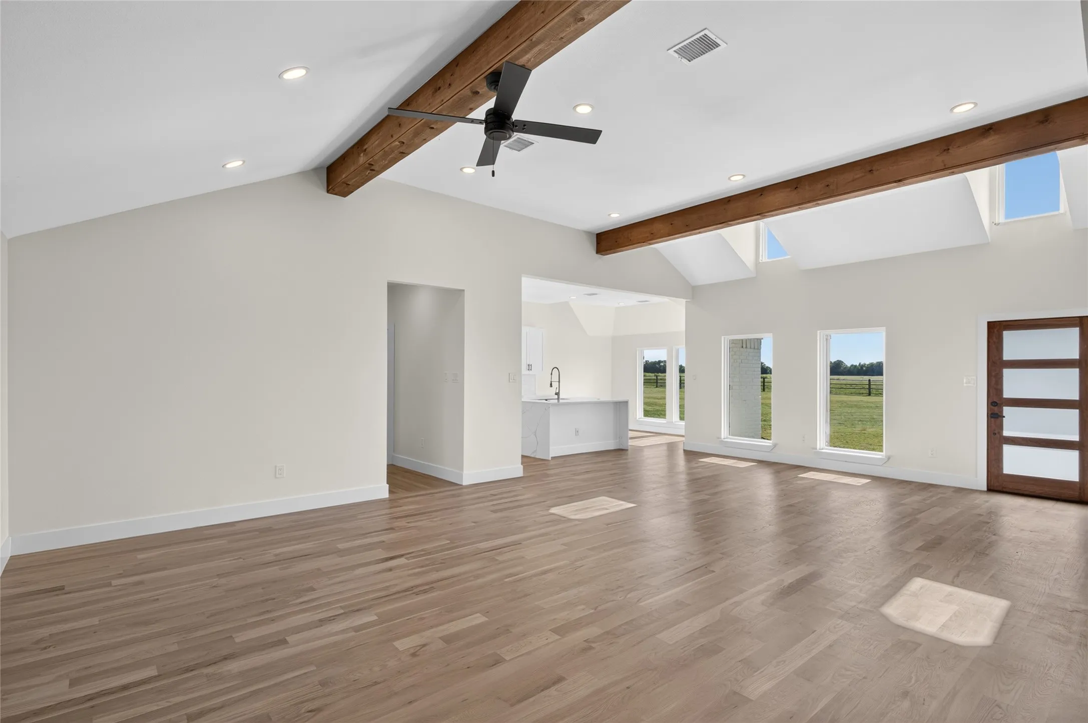 Spacious living area featuring wood-finish flooring, vaulted ceilings with exposed beams, and recessed lighting
