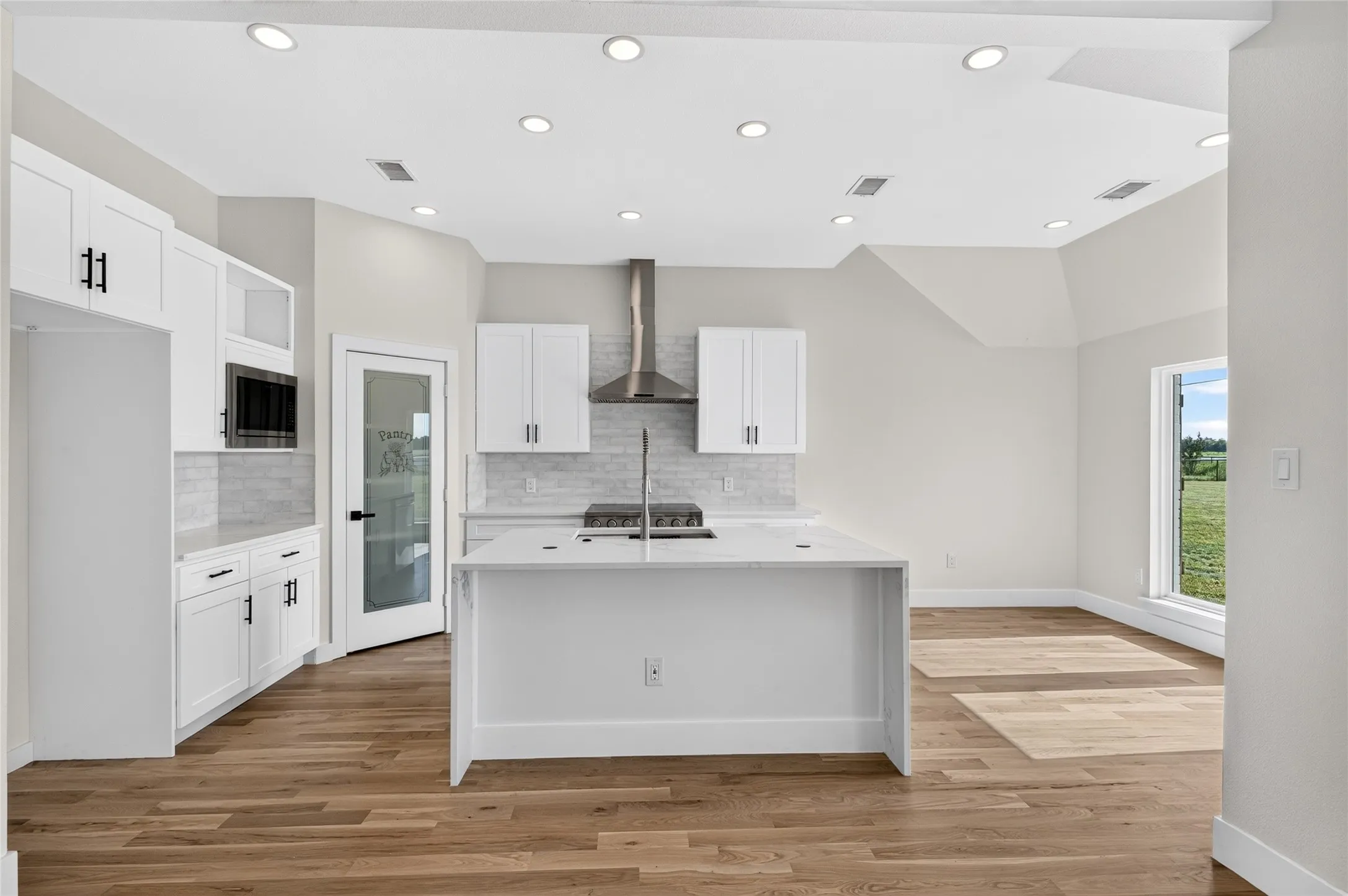 Modern kitchen featuring white cabinetry, a central island with an integrated sink, and wood-finish flooring