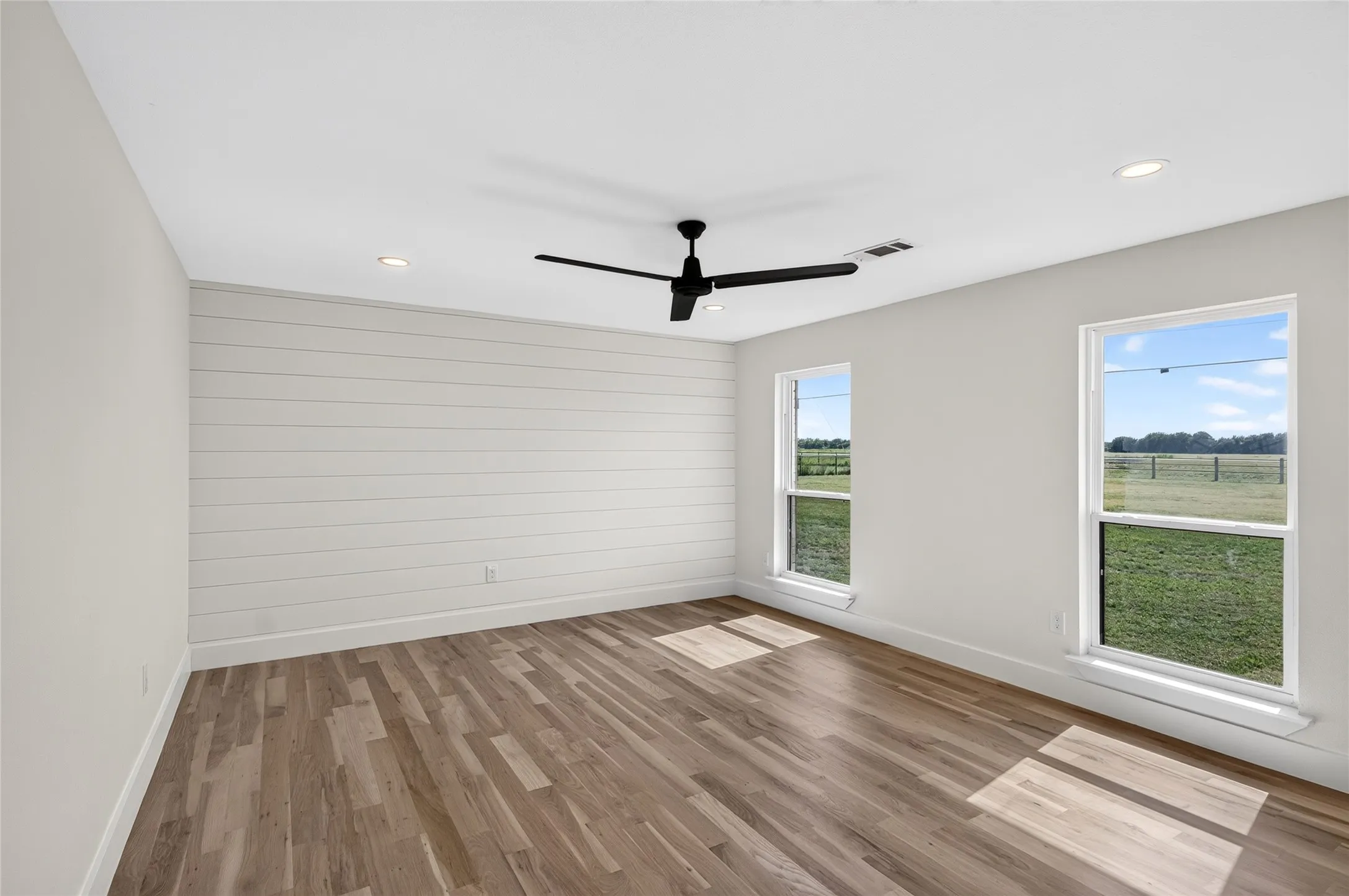 Spacious room featuring wood-finish flooring, a shiplap accent wall, a ceiling fan, recessed lighting, and two windows