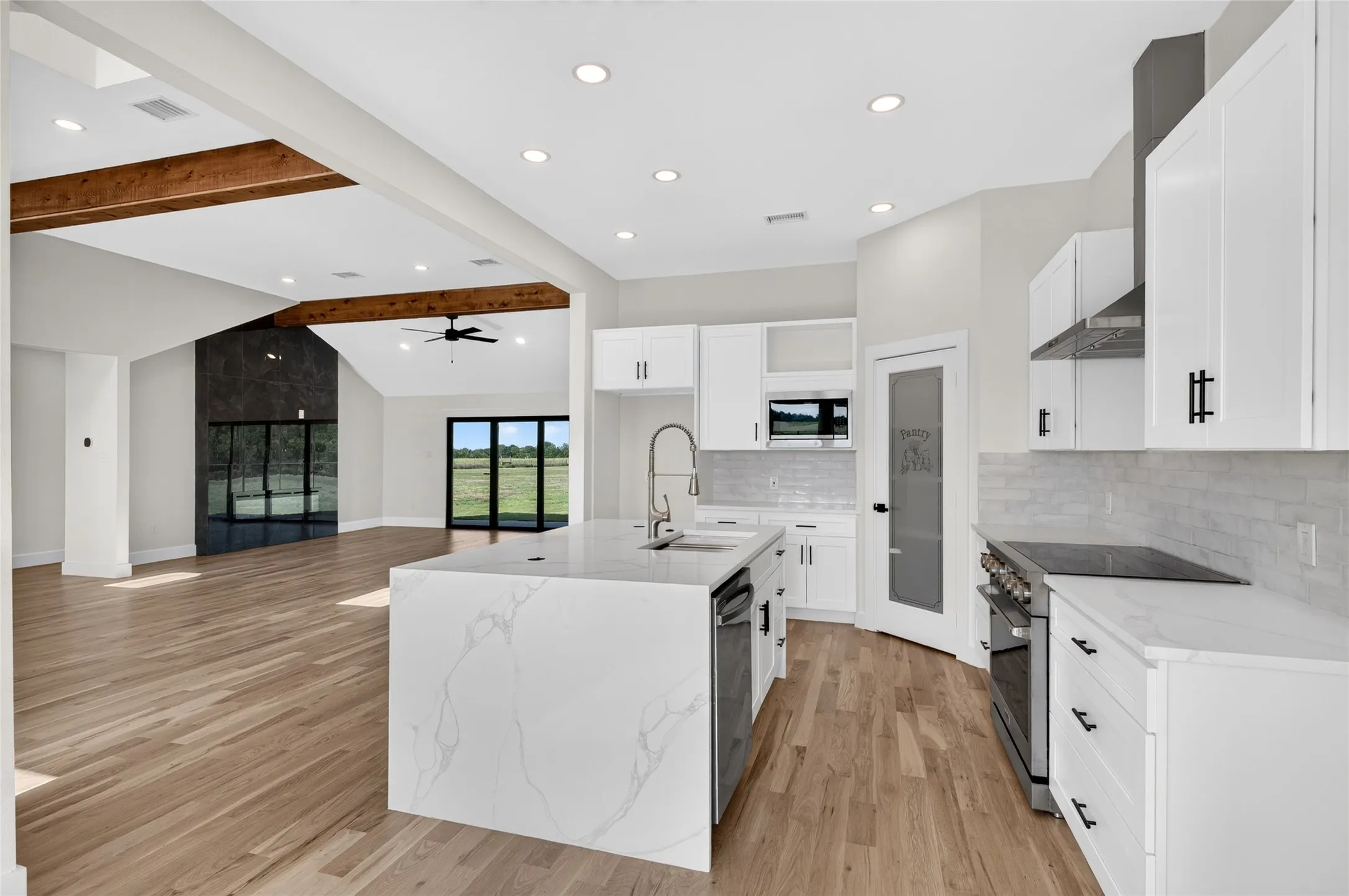 Open-concept kitchen featuring a waterfall island with an integrated sink, white cabinetry with matte black hardware, stainless steel appliances, and wood-finish flooring