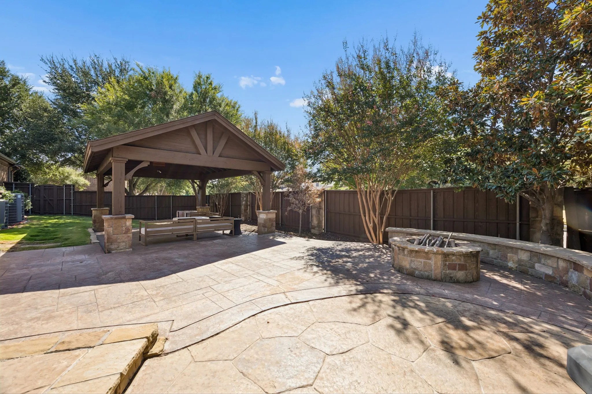 Patio with stamped concrete paving, covered pergola with stone accents, a built-in stone fire pit