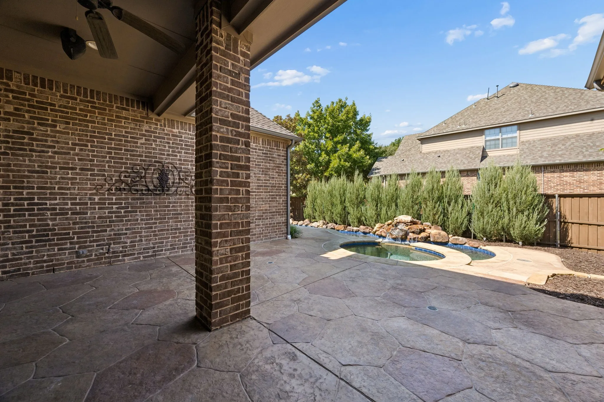 Covered patio with a ceiling fan, brick wall, and flagstone-style concrete flooring
