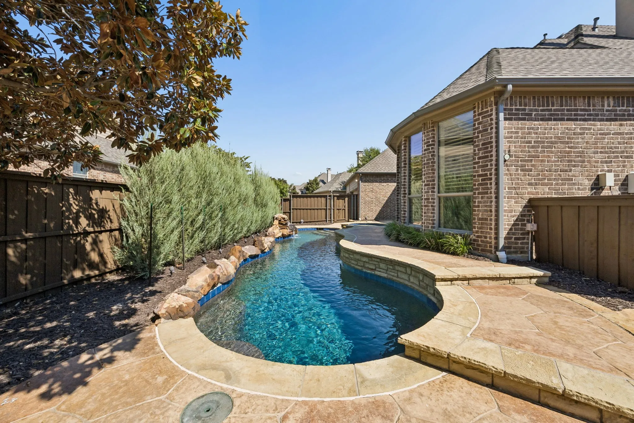 Freeform swimming pool with rock coping and integrated spa, surrounded by stamped concrete decking