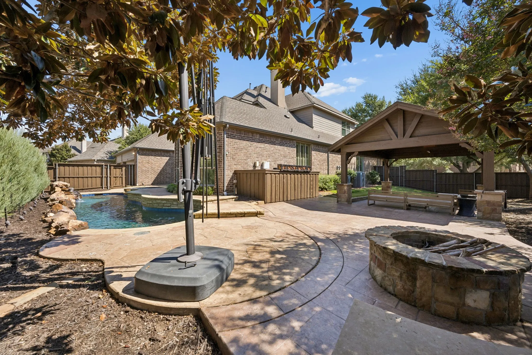 Swimming pool with rock water feature, stone fire pit, stamped concrete patio, and covered gazebo