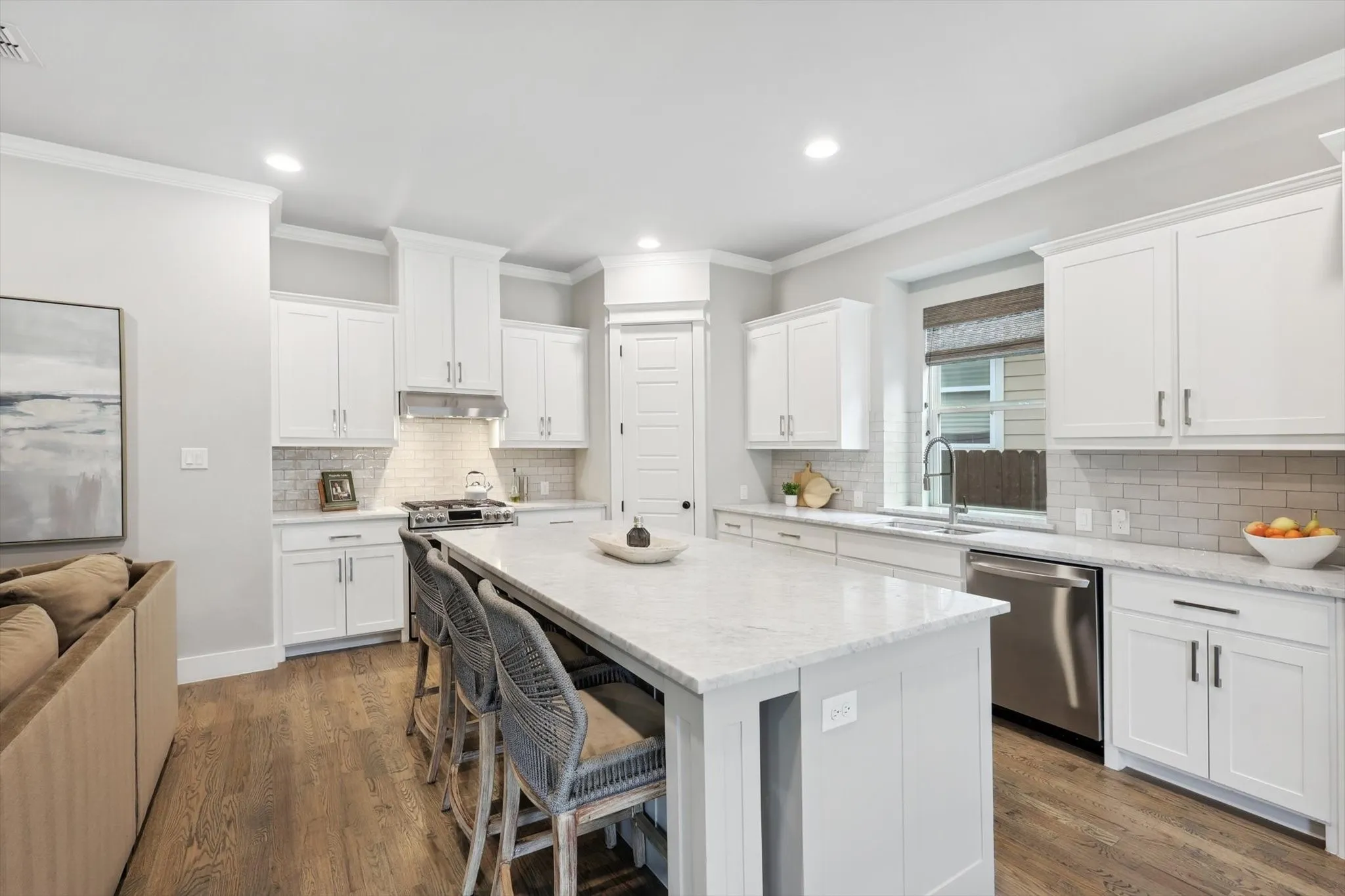 Kitchen featuring white cabinetry, light-toned countertops, a subway tile backsplash, stainless steel appliances, and wood-finish flooring