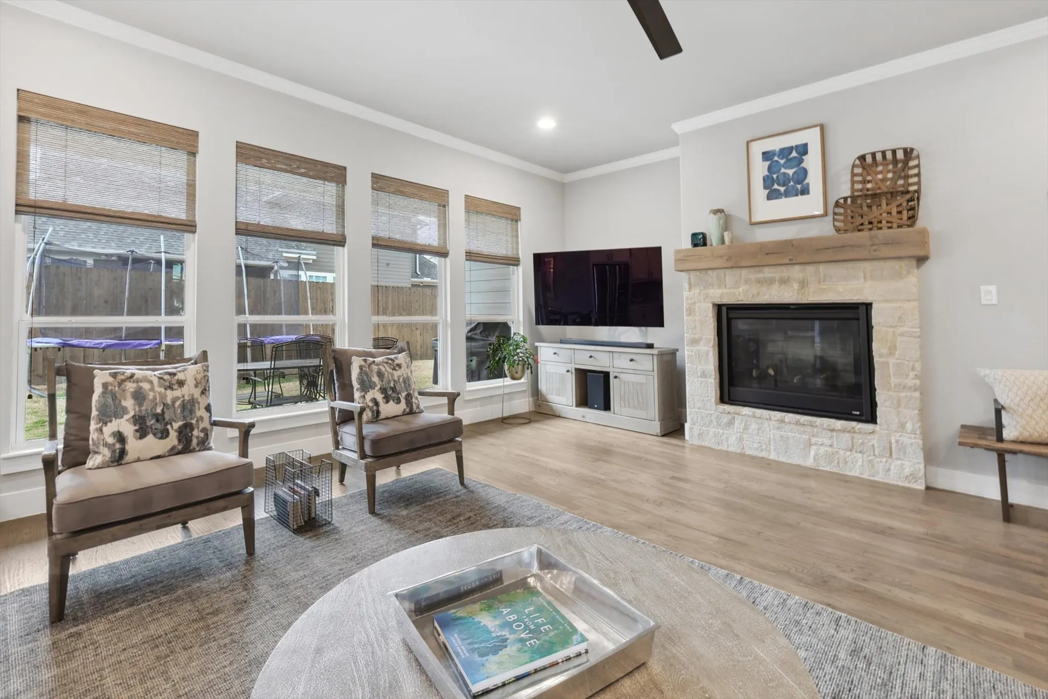 Living area featuring wood-finish flooring, a stone-surround fireplace with a wood mantle, and multiple windows with woven shades