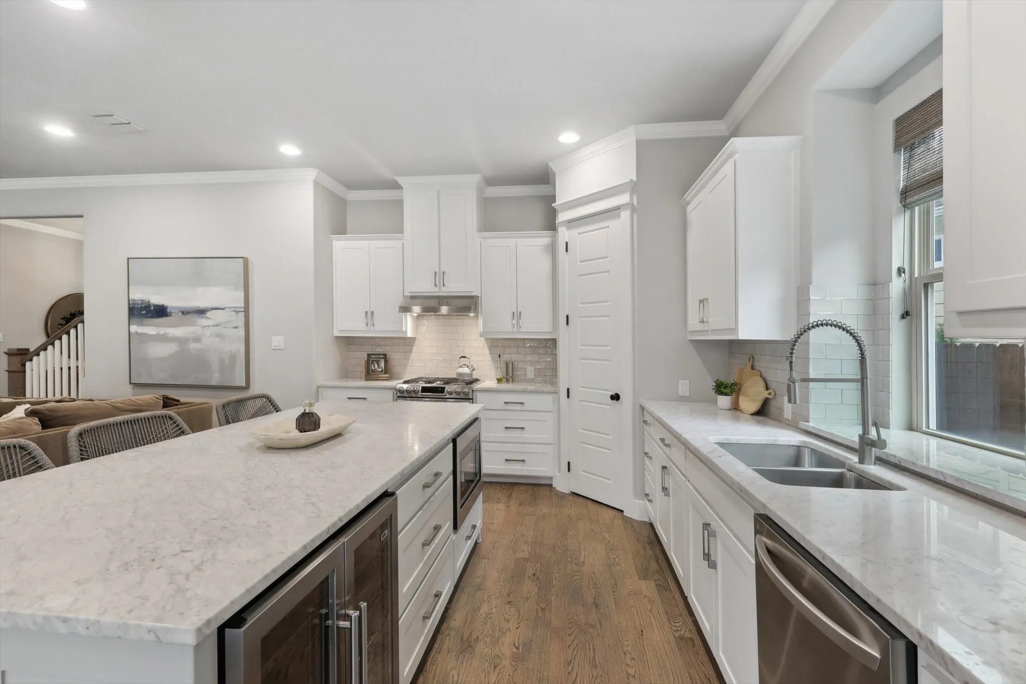 Kitchen featuring a large island with integrated beverage cooler, stainless steel appliances, white cabinetry, and wood-finish flooring