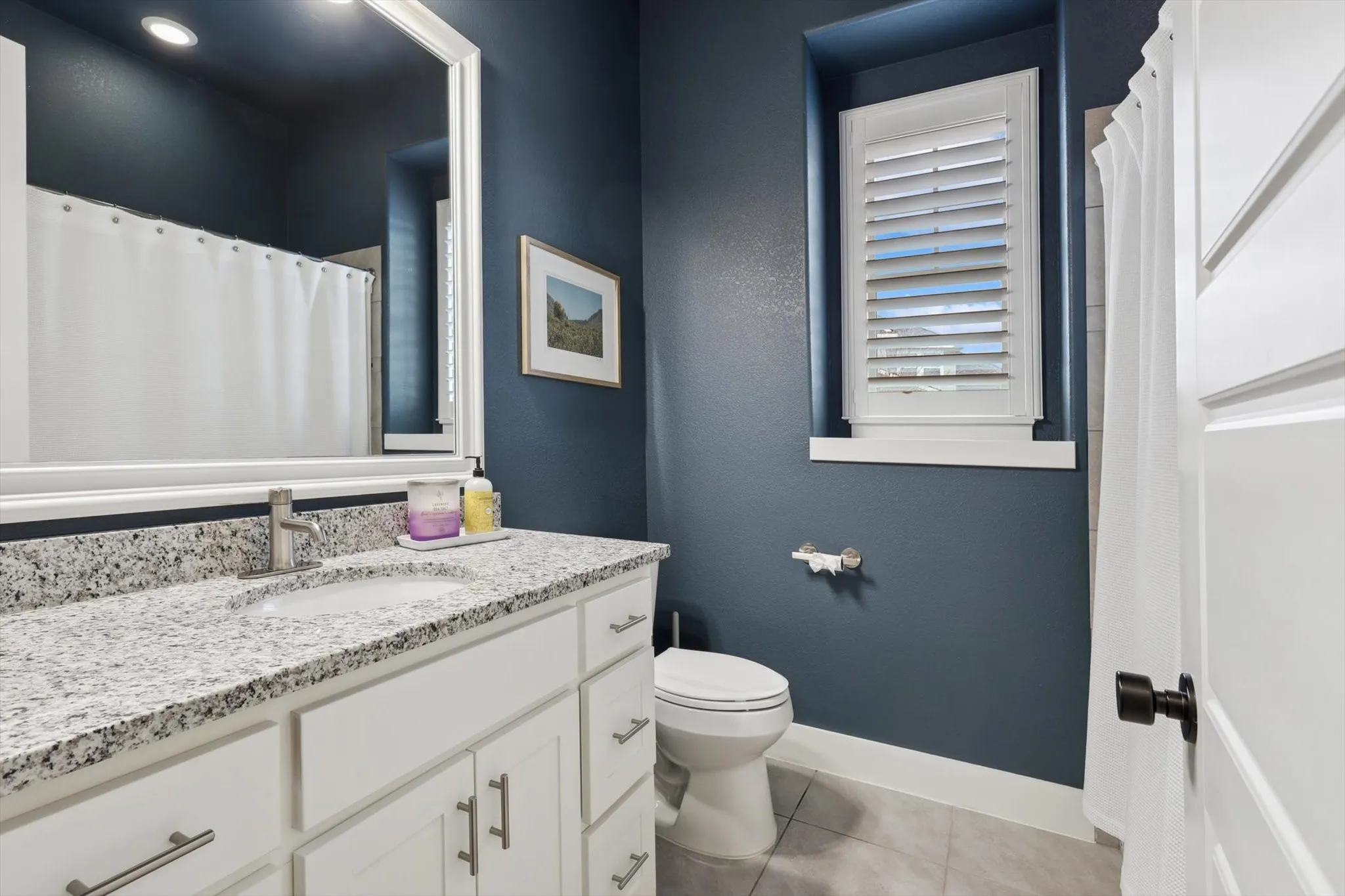 White shaker vanity with a granite countertop, undermount sink, and brushed nickel faucet