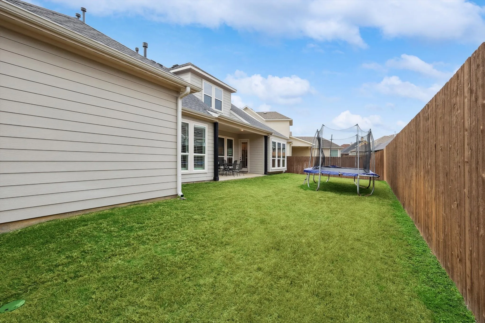 Expansive backyard featuring a manicured lawn, full privacy fencing, and a covered patio area