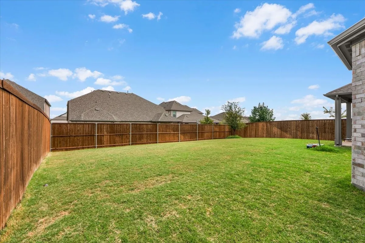 Expansive grassy lawn with a wood privacy fence and a partial brick exterior