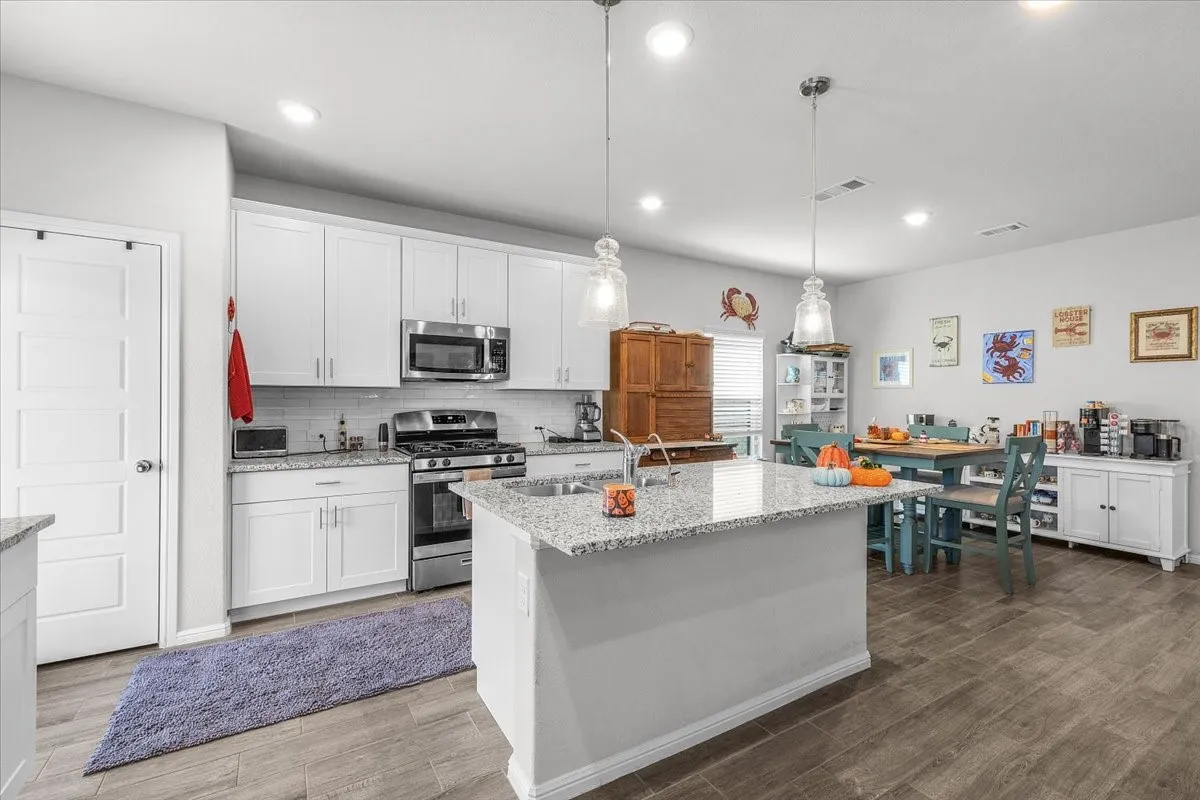 Spacious kitchen featuring an island with a sink, stainless steel appliances, white cabinetry, granite countertops, and wood-finish flooring