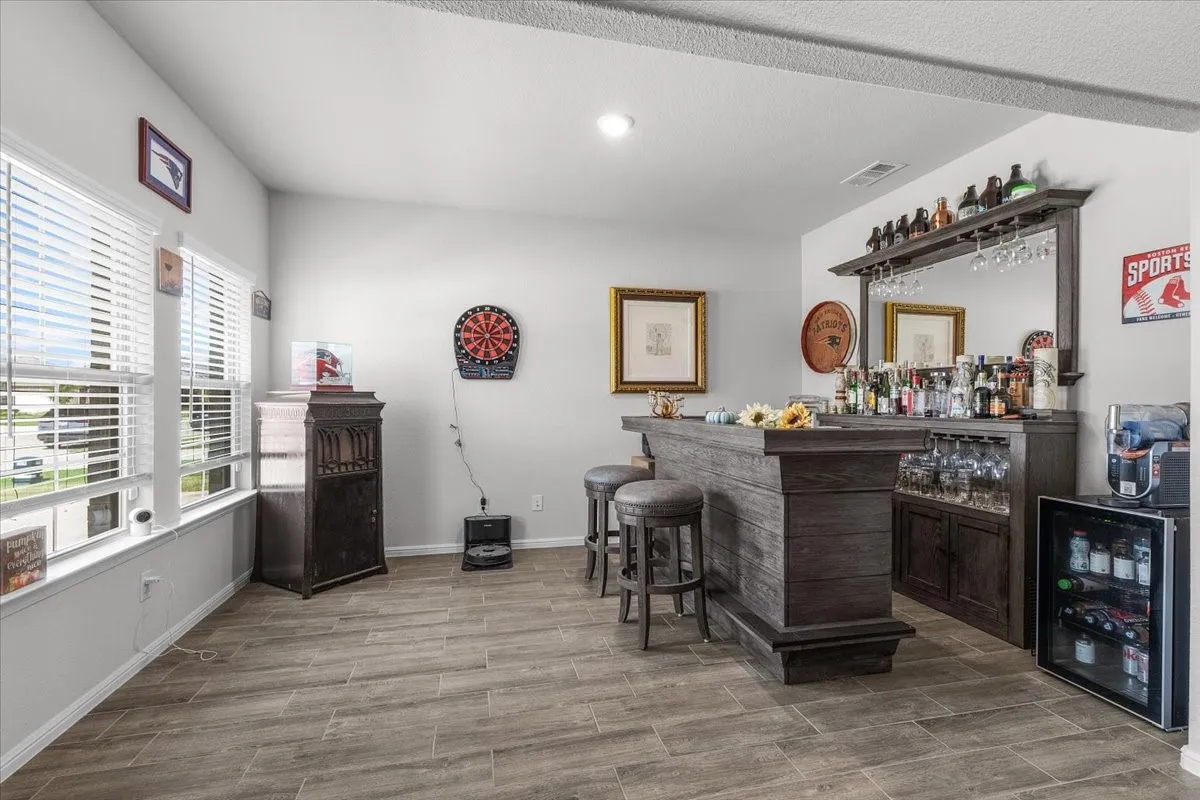 Spacious room featuring wood-finish flooring, multiple windows with blinds, a built-in bar, and recessed lighting