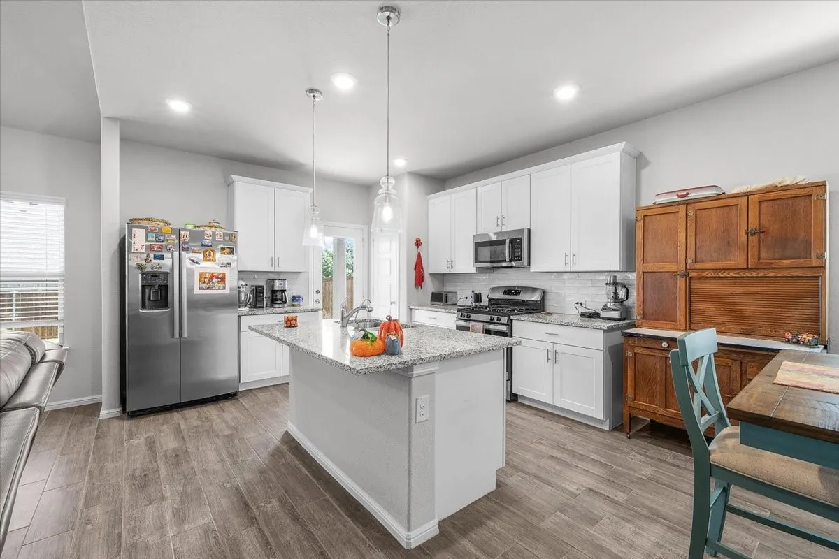 Kitchen featuring an island with a sink, white cabinetry, granite countertops, and wood-finish flooring