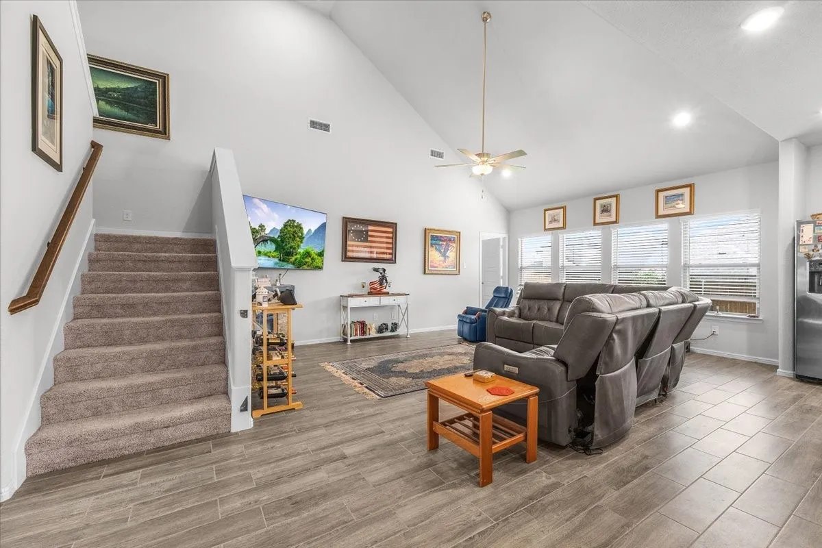 Vaulted ceiling, recessed lighting, wood-look tile flooring, carpeted staircase with wood handrail, and multiple windows with blinds
