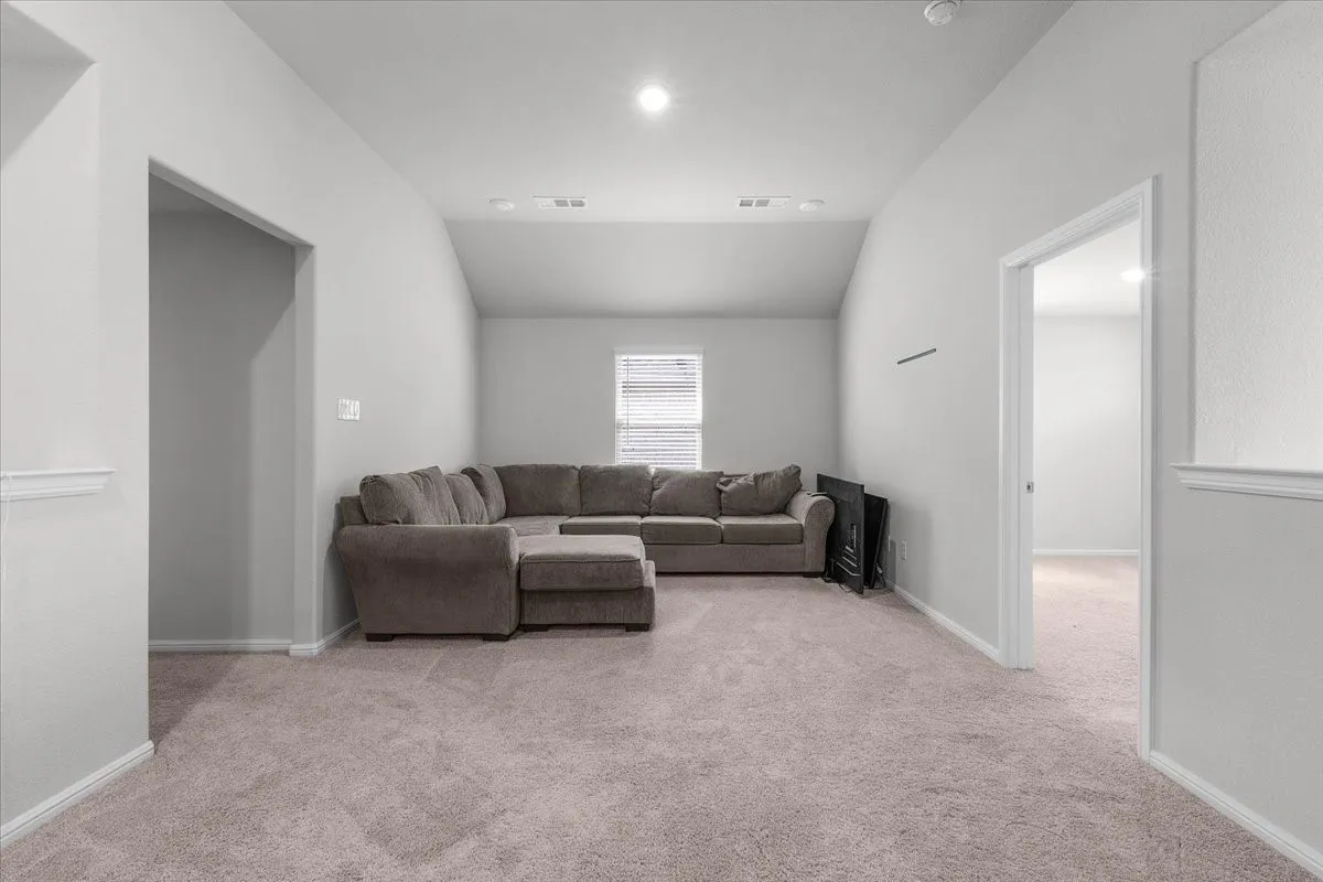 Spacious room with vaulted ceiling, neutral gray wall tones, light-colored carpeting, and a window with blinds