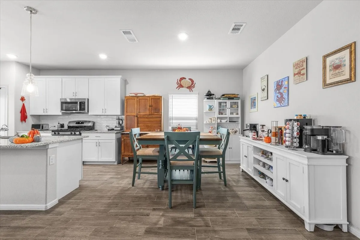 Kitchen featuring white cabinetry, stainless steel appliances, a center island with a stone-finish countertop, and wood-finish flooring