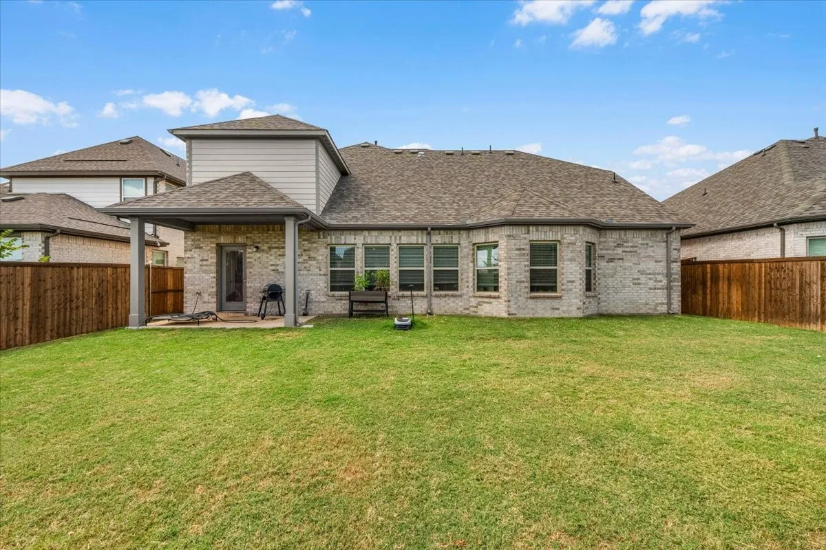 Expansive grass lawn with a covered patio featuring a pitched roof and brick facade