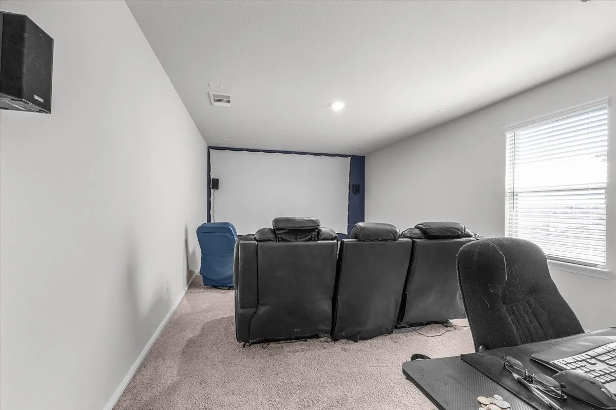 Media room featuring a projector screen, wall-mounted speaker, recessed lighting, and a window with horizontal blinds
