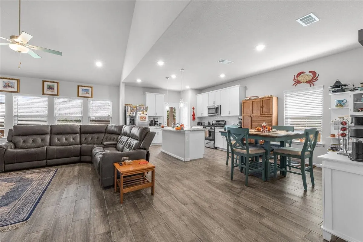 Vaulted ceiling, wood-finish flooring, recessed lighting, white cabinetry, and stainless-steel appliances