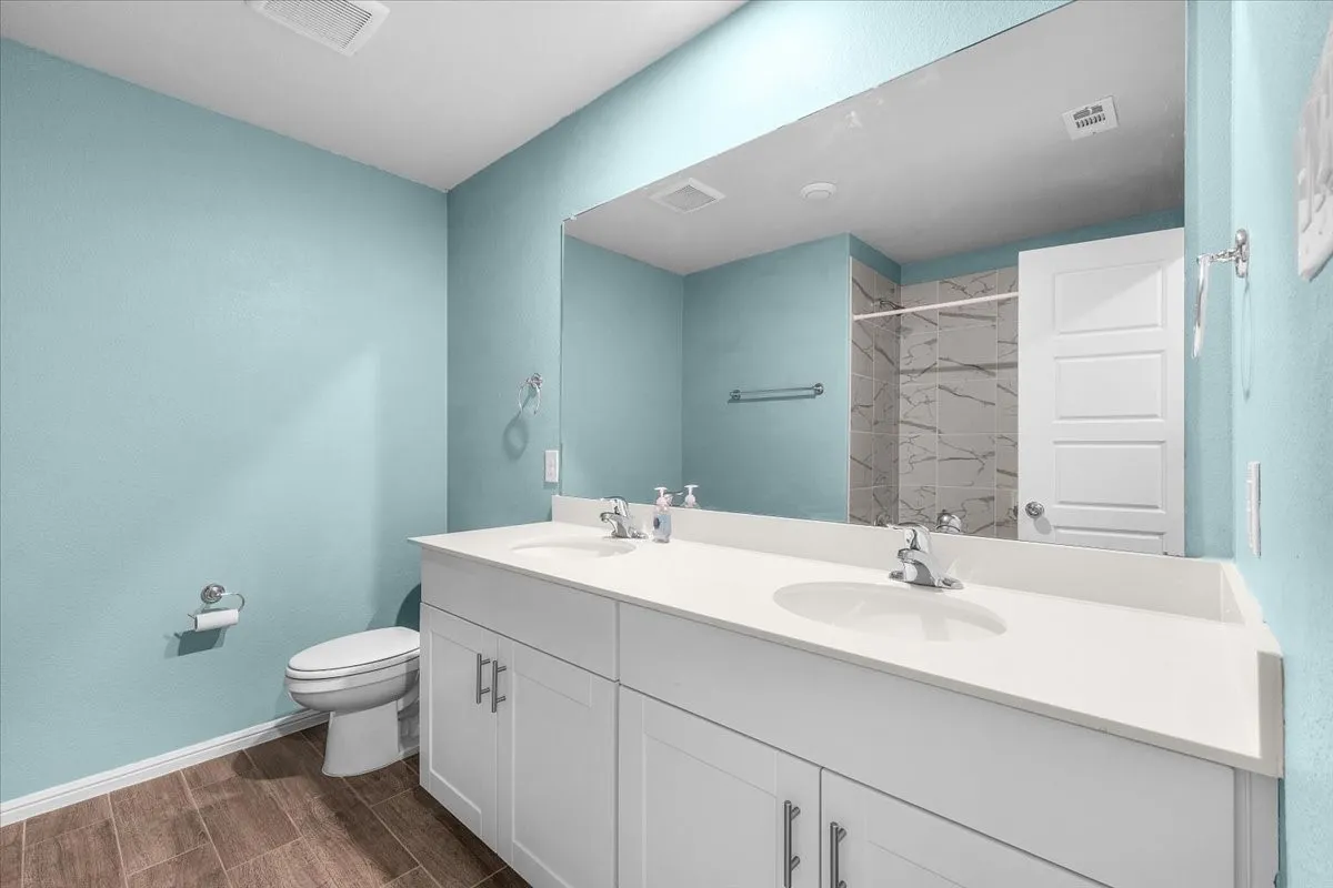 Dual vanity with integrated sinks, white cabinetry, wood-finish flooring, and a tiled shower enclosure