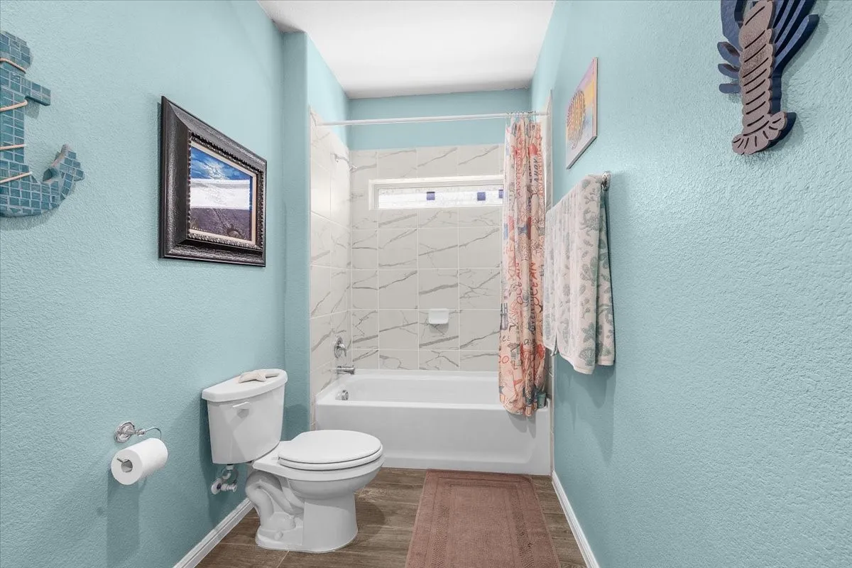 Bathtub with tiled surround, wood-finish flooring, and a single toilet