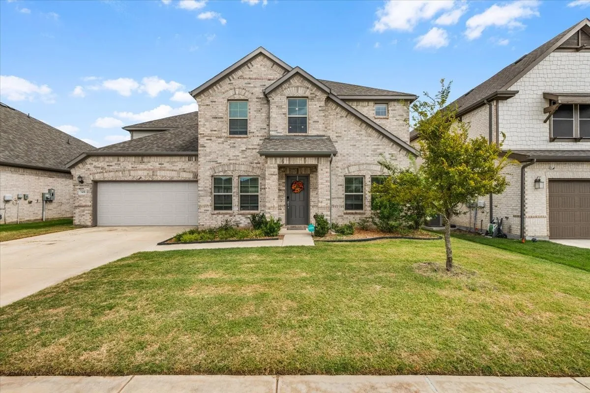 Brick facade with a gabled roofline, featuring an attached garage, landscaped front yard, and a paved driveway